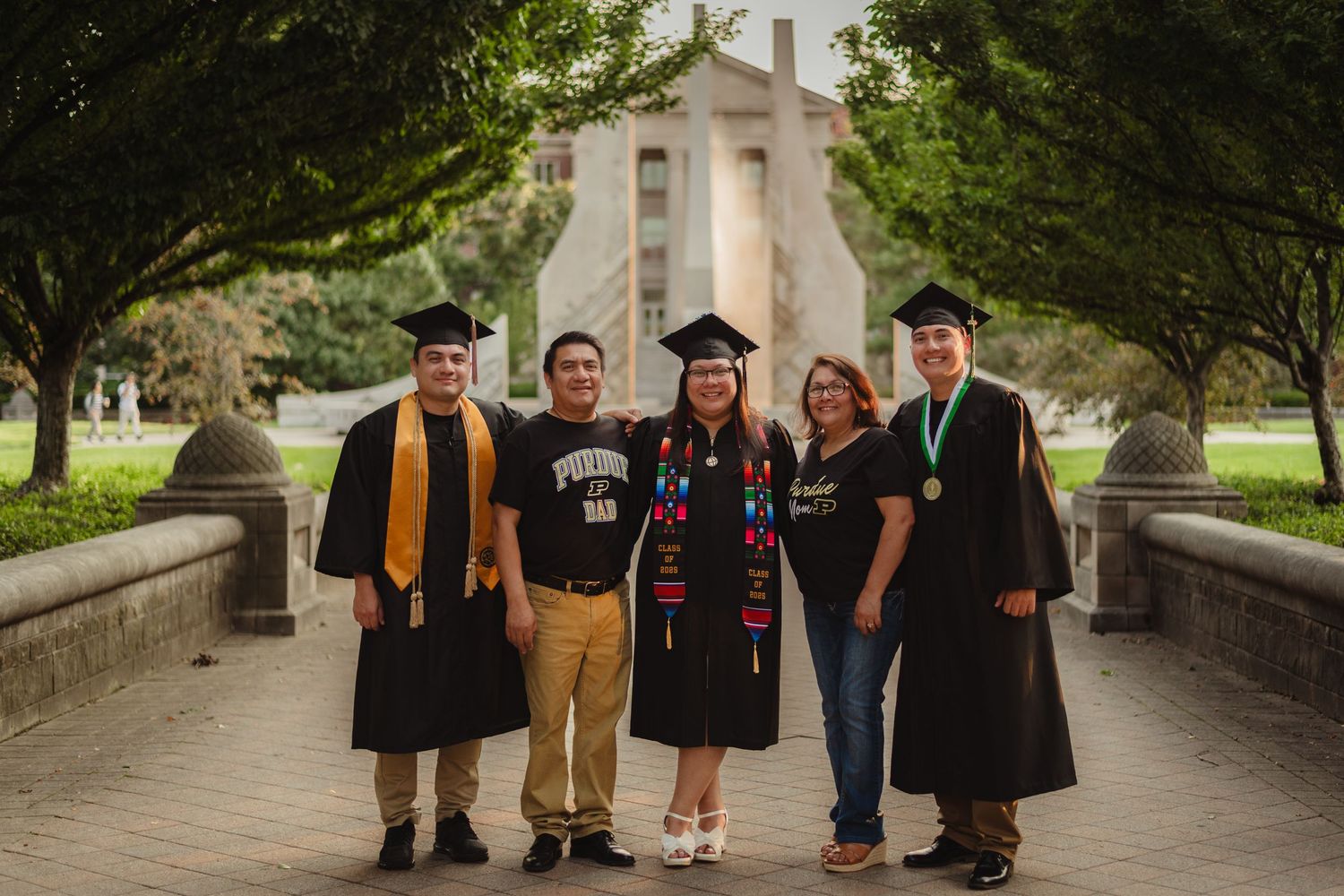 A group of graduates in caps and gowns walk along a tree-lined path during commencement ceremonies  at Purdue Campus in West Lafayette, IN.