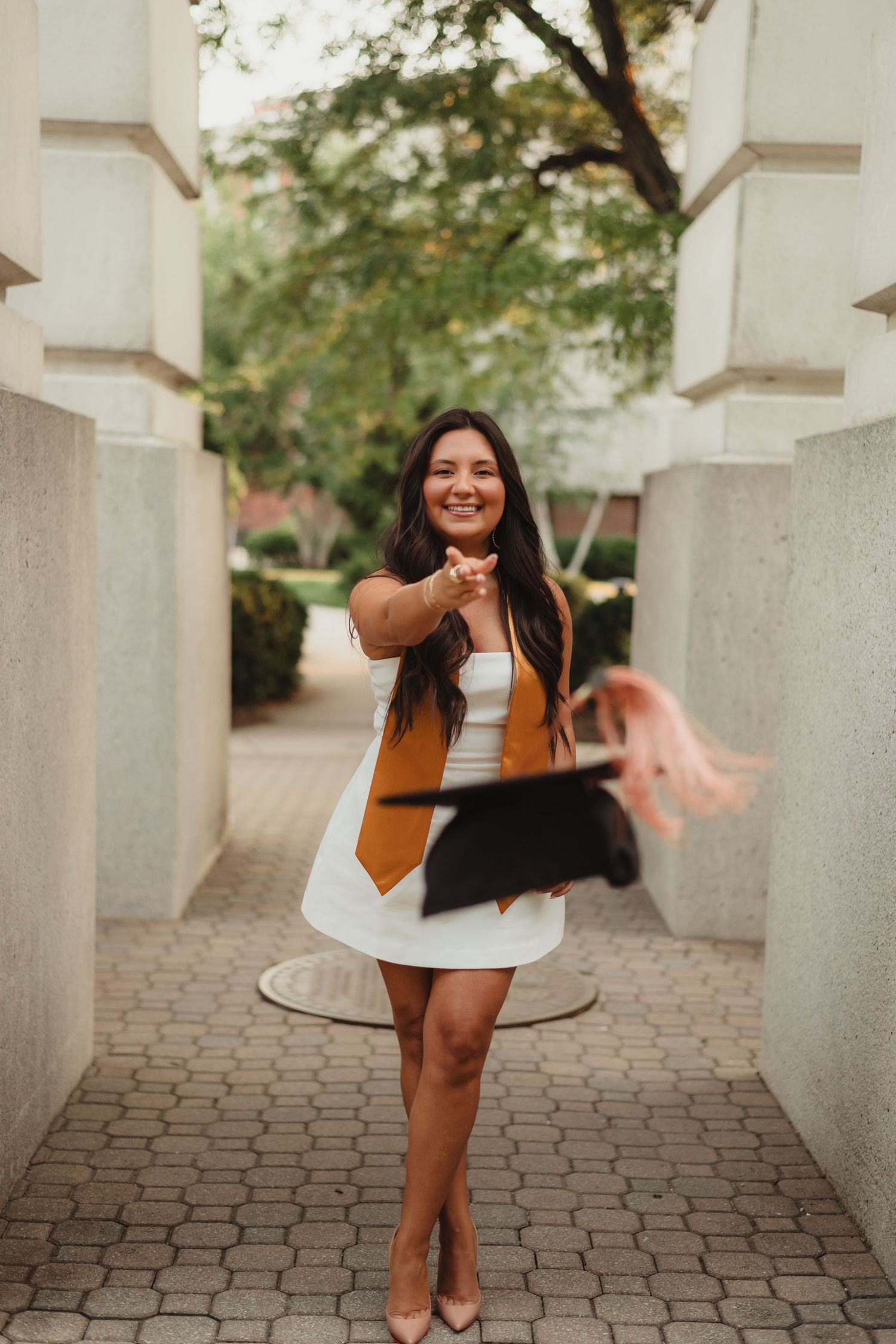 A person dances and twirls joyfully between architectural columns on a brick pathway  at Purdue Campus in West Lafayette, IN.