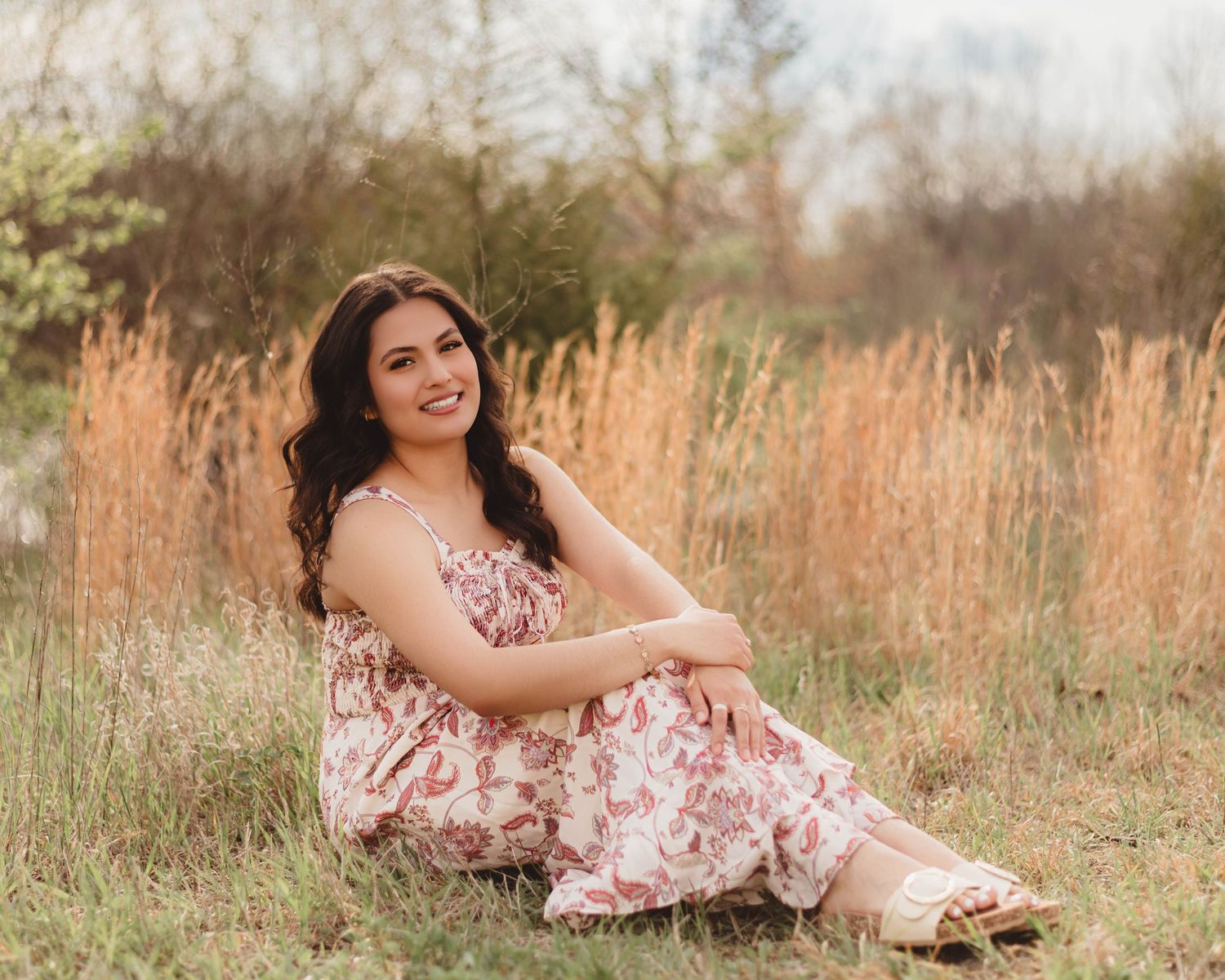 High School Senior in floral maxi dress sitting gracefully in a golden grass field for senior portrait photography in Lafayette, Indiana.