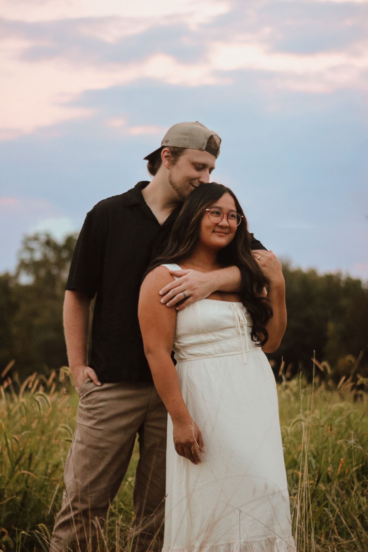 A romantic couple embraces in a golden field at sunset creating an intimate outdoor portrait series.