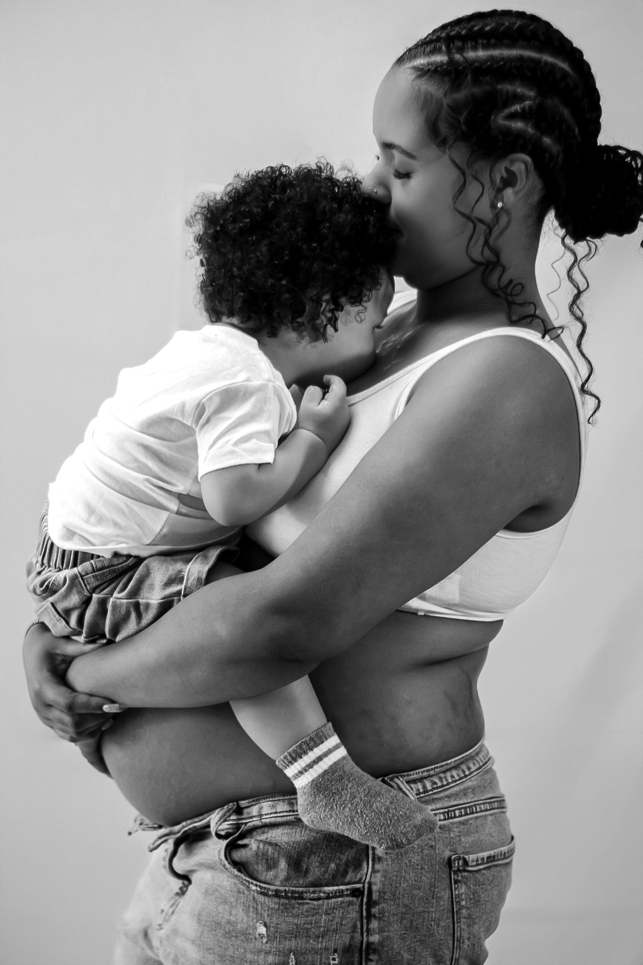 A tender black and white portrait of a parent embracing and kissing their young child with curly hair.