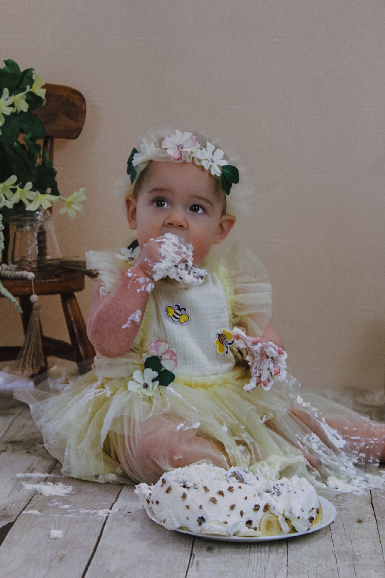 A baby wearing yellow dress tastes cake frosting during a smash cake photo session.