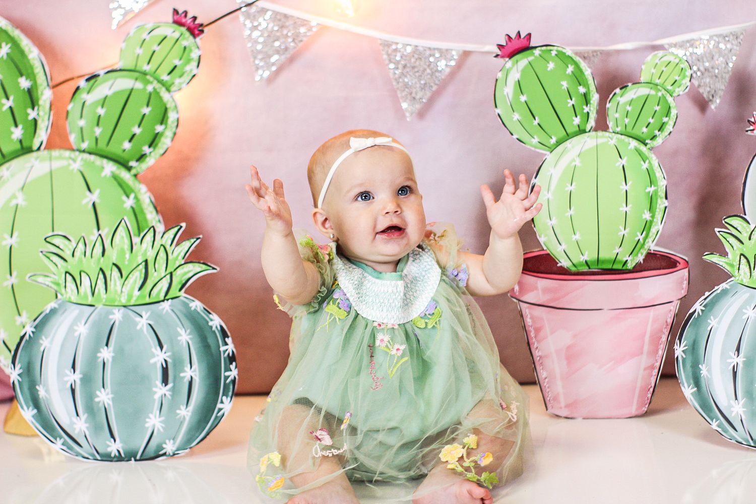 Festive cactus-themed photo setup with mint green decor and silver banner bunting against a pink backdrop.