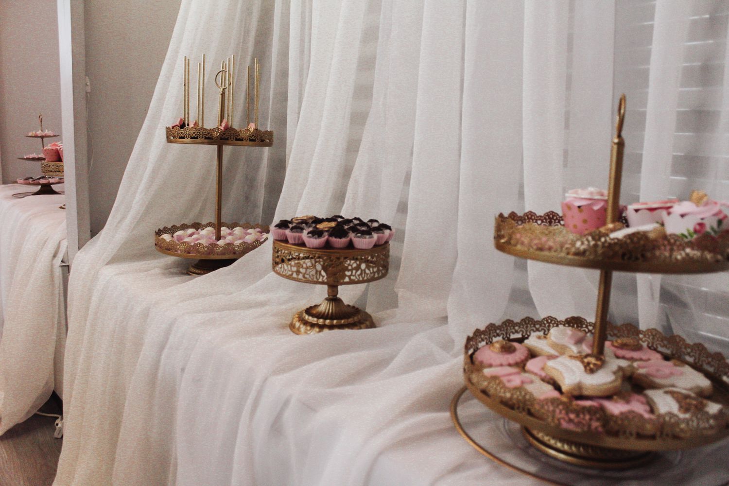 Elegant dessert display with tiered stands and pink treats against white draping.
