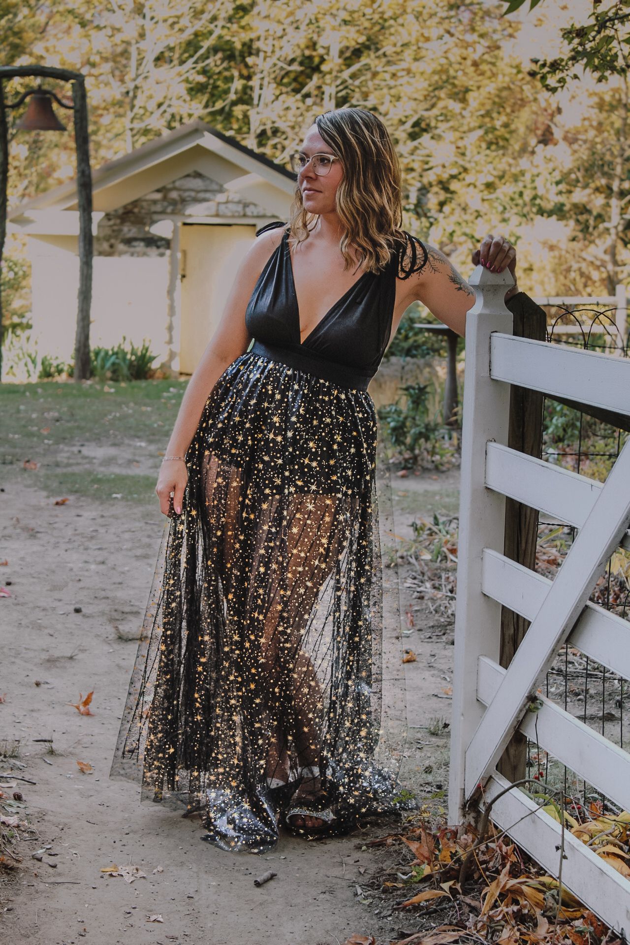 A sparkly black mesh dress styled with a deep v-neck against a rustic white fence and autumn backdrop.