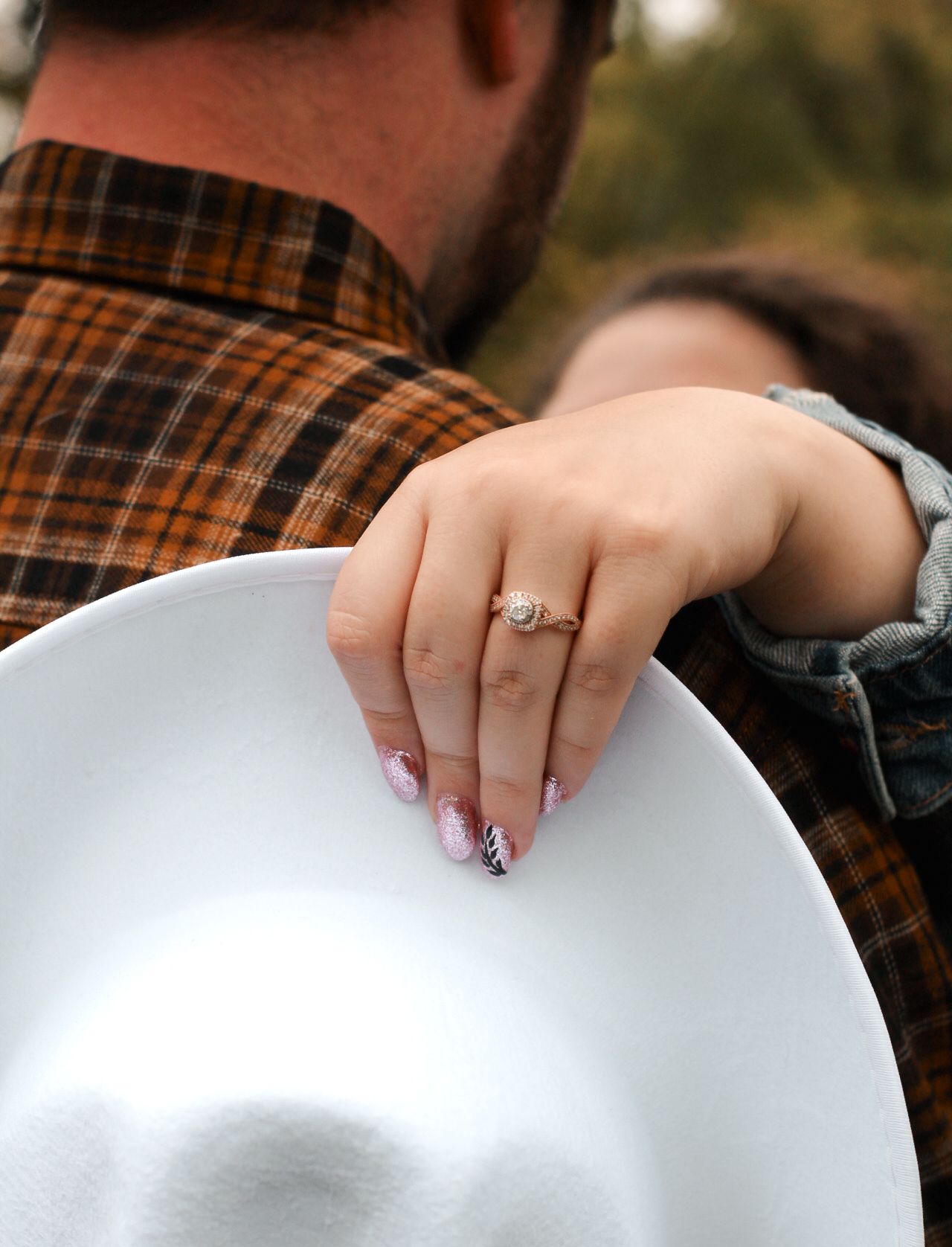 Hand resting on a white cowboy hat showing an engagement ring.