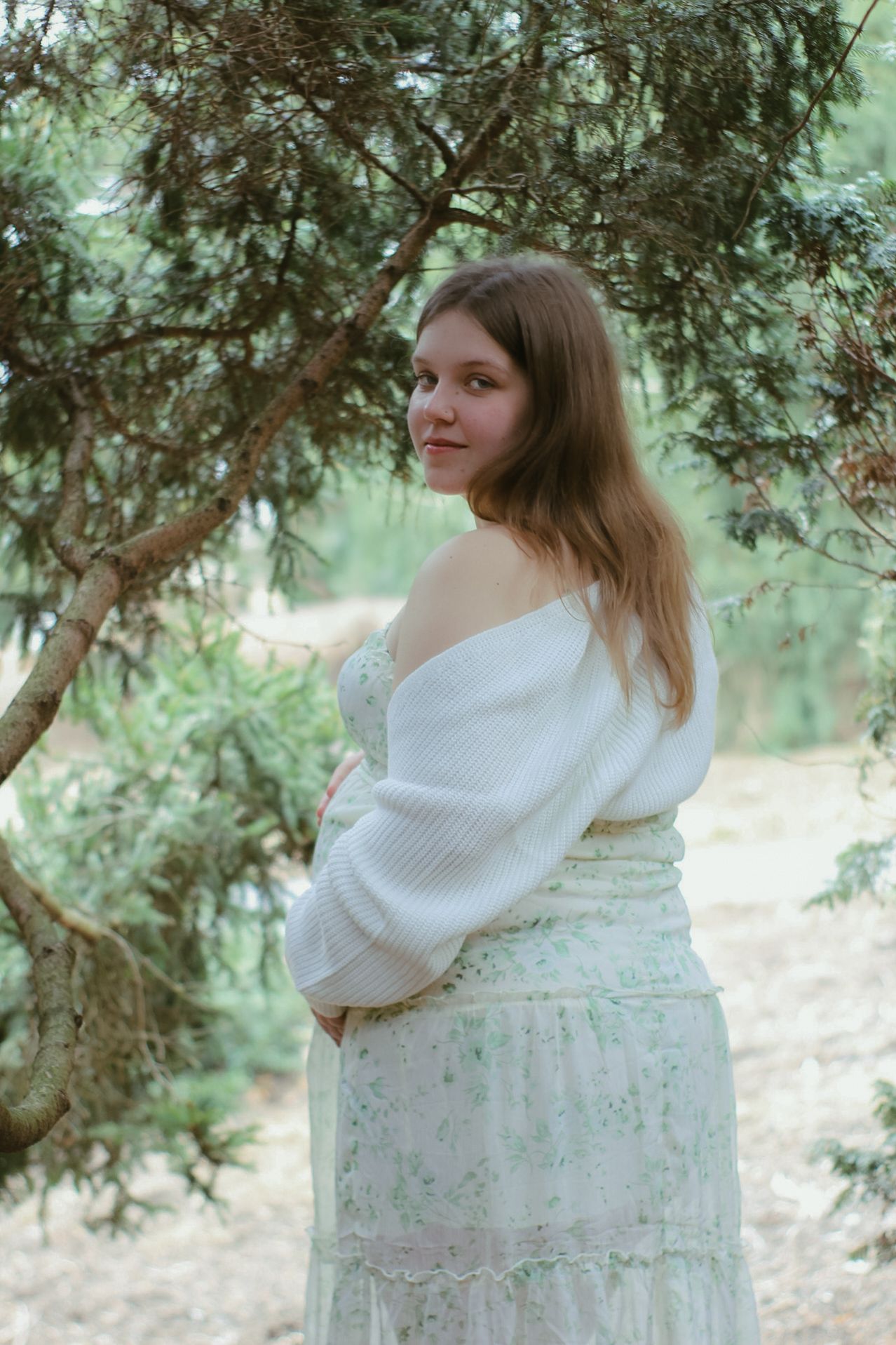 A maternity portrait in a dreamy forest setting with soft natural lighting.