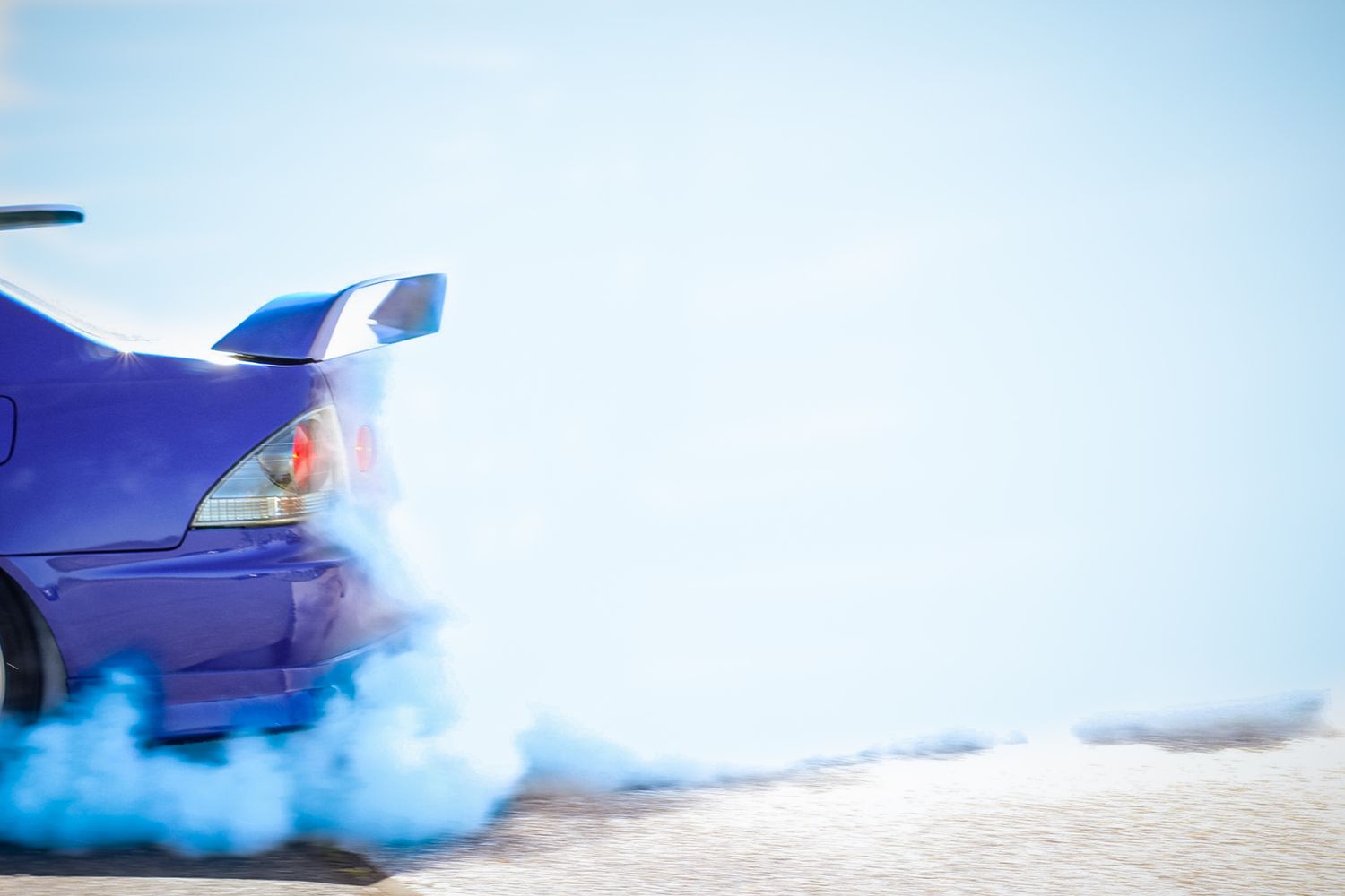 Blue smoke billows around a car against bright white background.