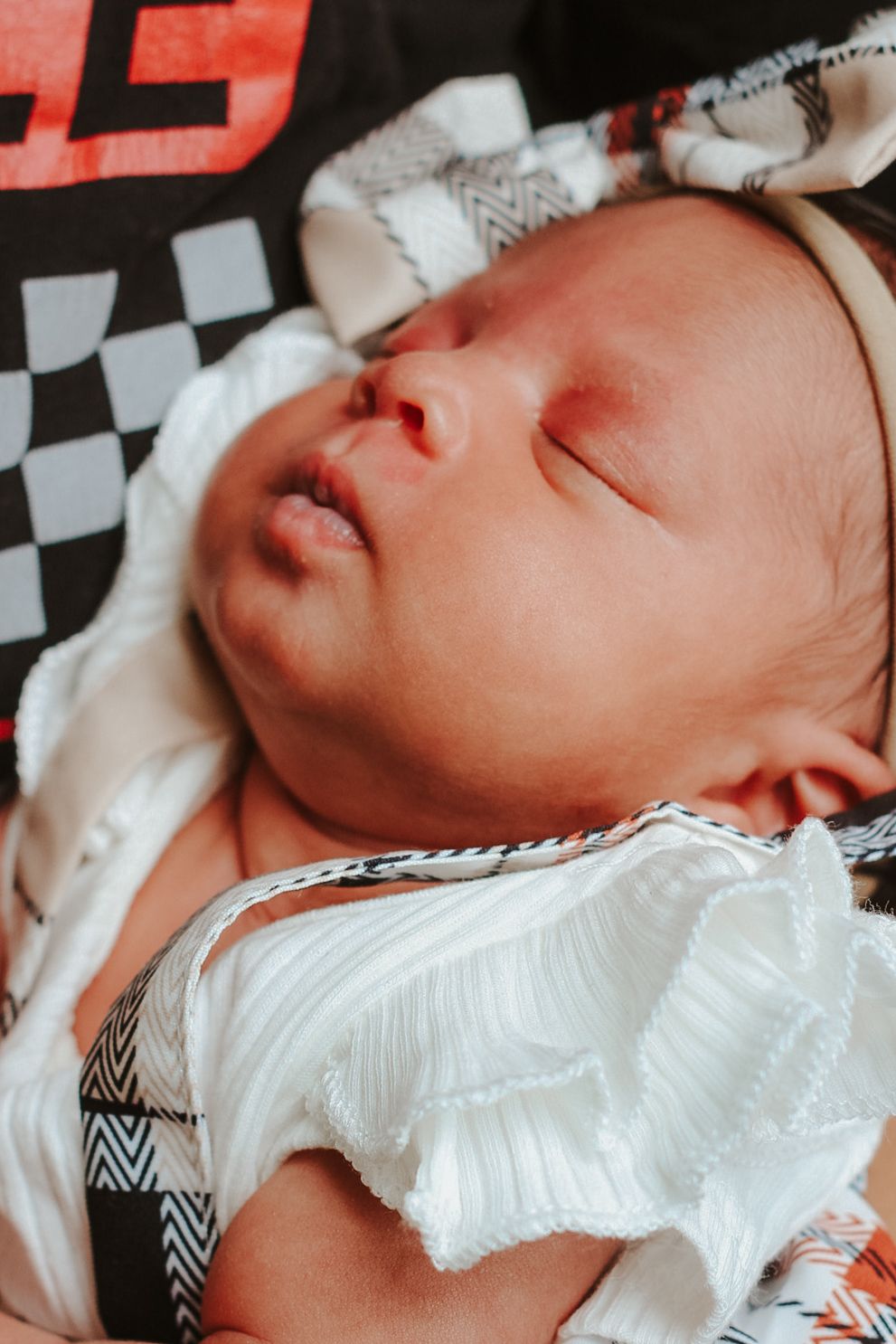 A sleeping newborn baby wearing white clothing rests peacefully on a black and white patterned blanket.