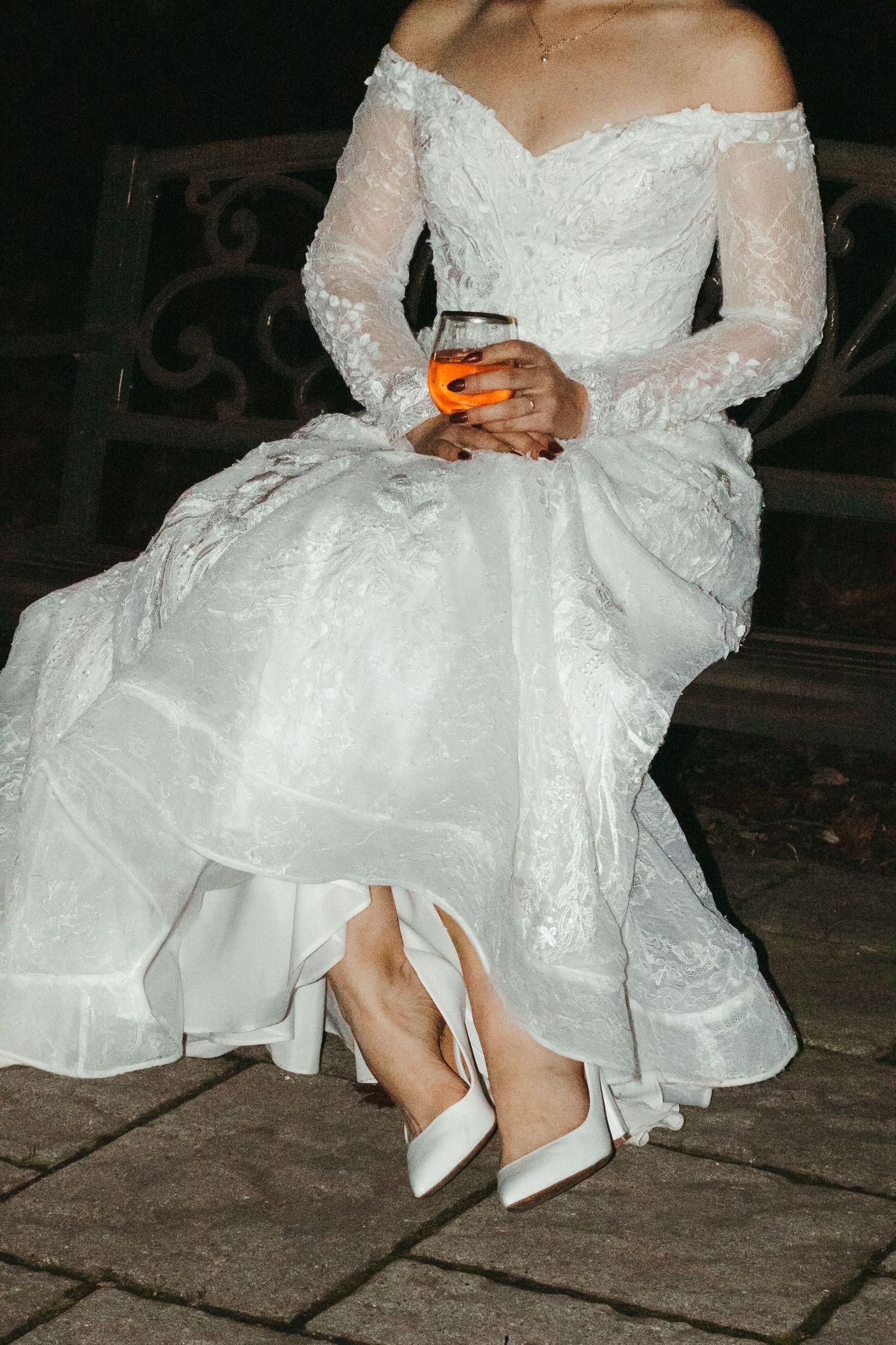 Close-up details of a bride's white lace wedding dress and heels on stone pavement.