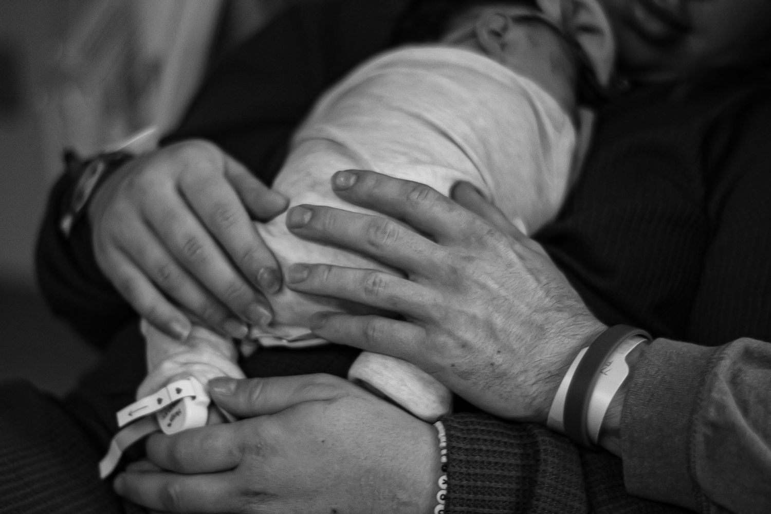 Close-up of hands gently holding a newborn baby wrapped in white cloth.