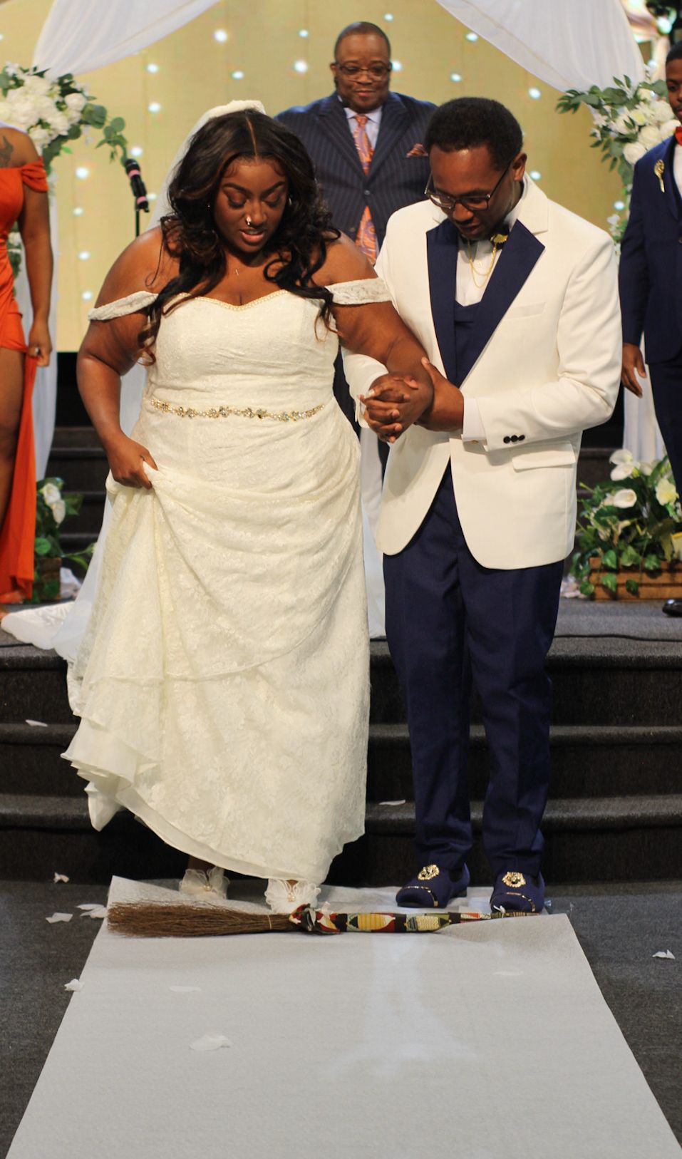Wedding couple performing traditional ceremony activities on stage with decorative backdrop.
