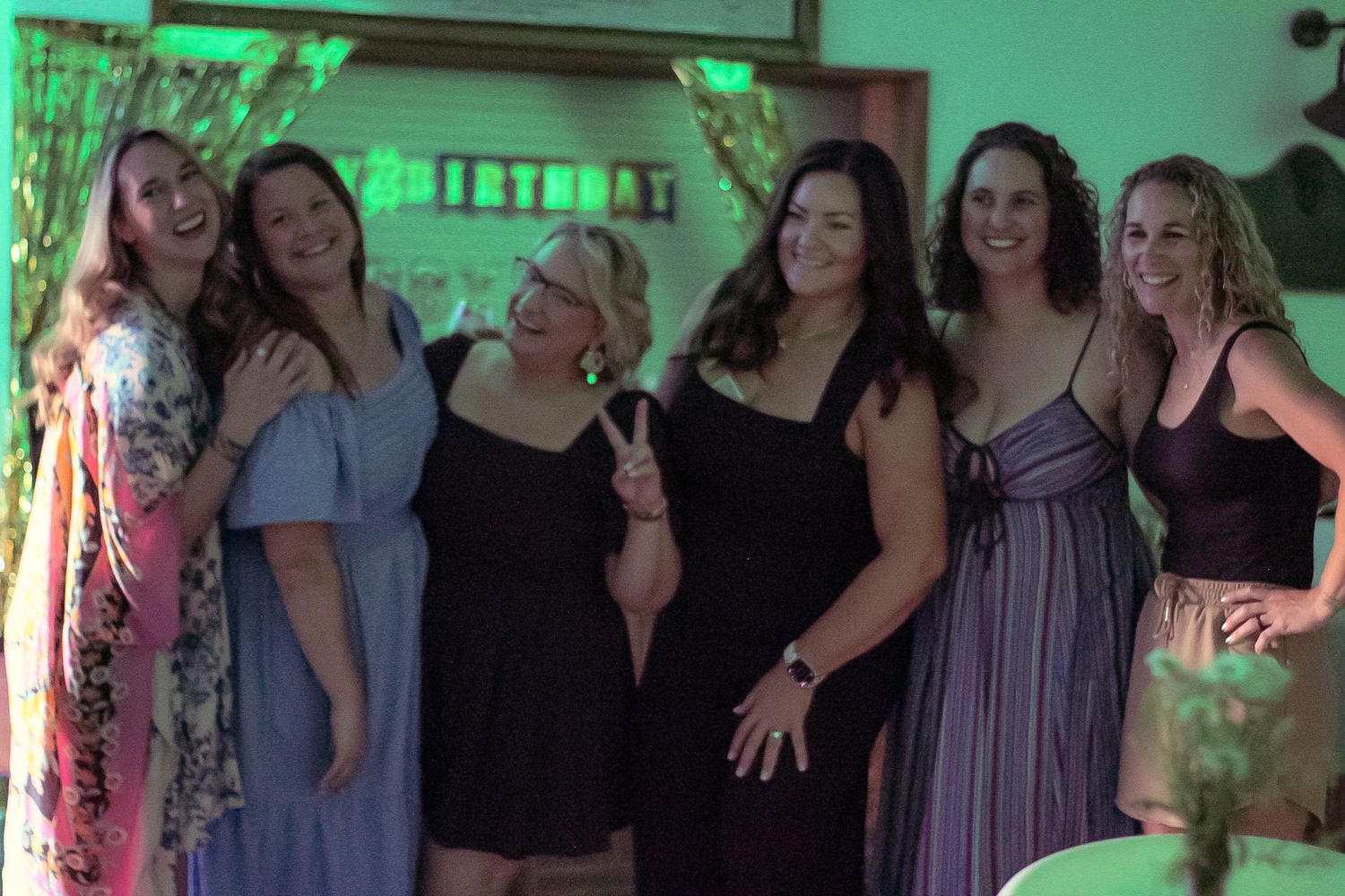 A group of friends pose together at a party wearing cocktail dresses in various colors and styles.