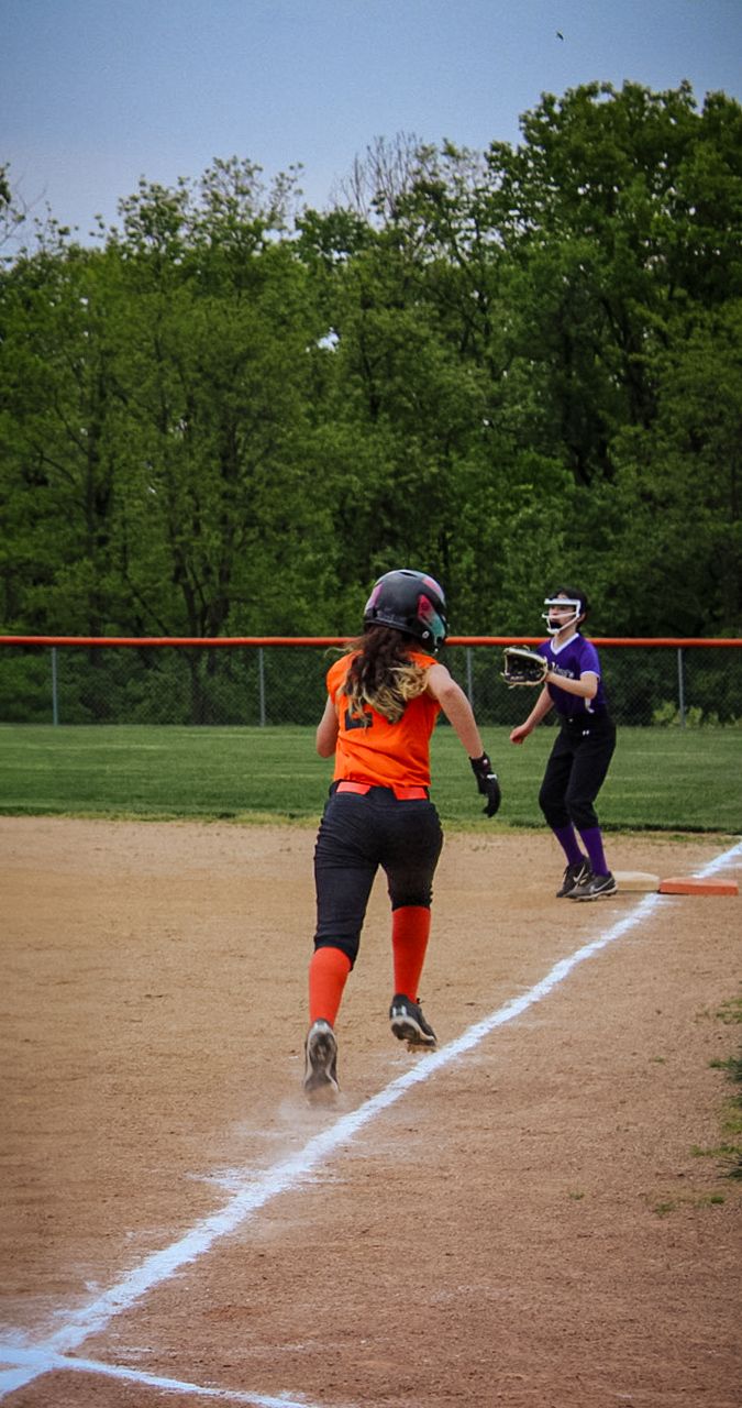 Softball player in orange and black uniform running toward first base during game.