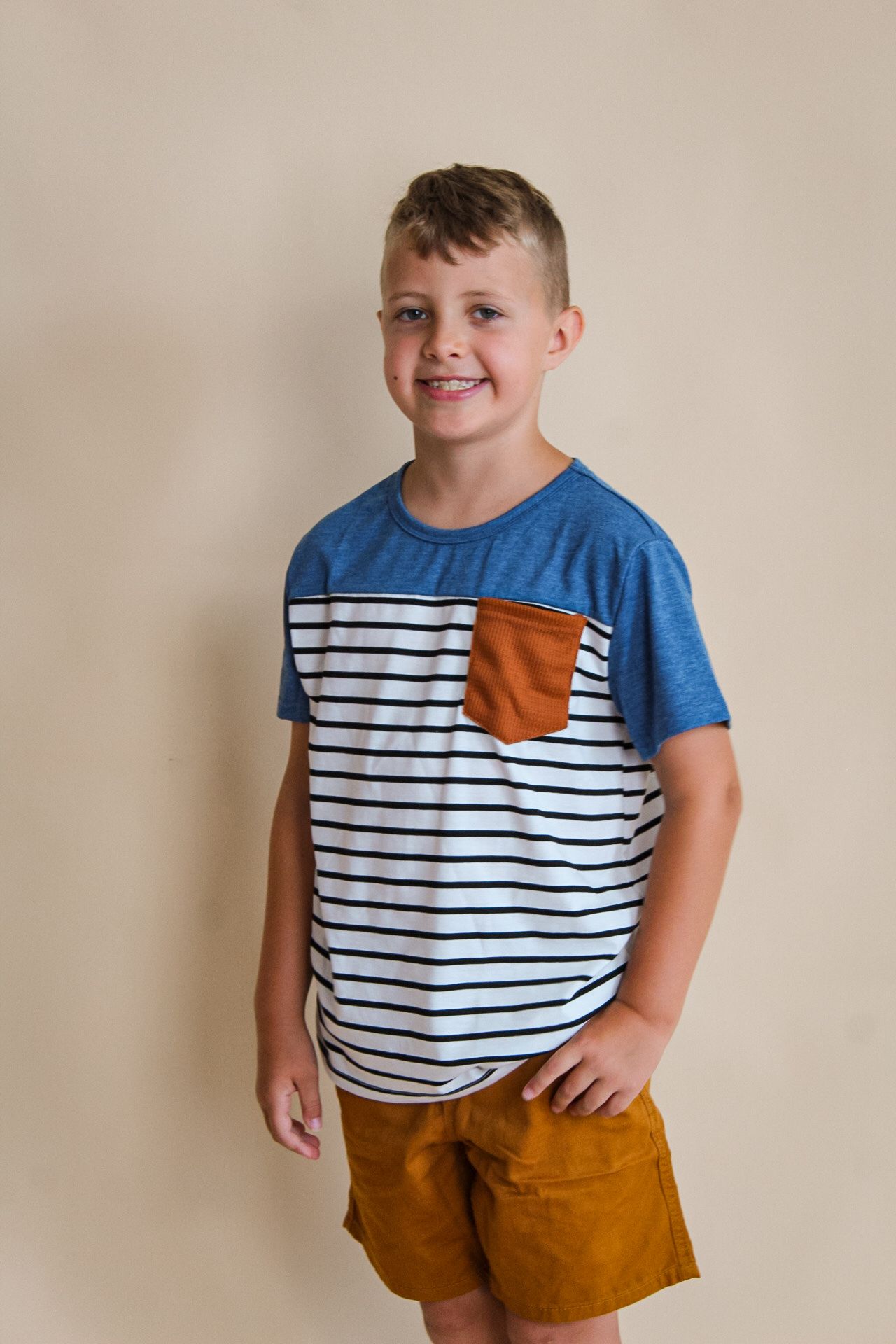 Young person in striped blue t-shirt with orange pocket standing against beige background.