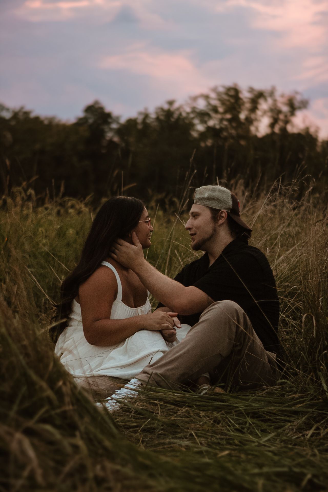 A couple lies together intimately in a field of tall grass at sunset during a romantic outdoor photoshoot.