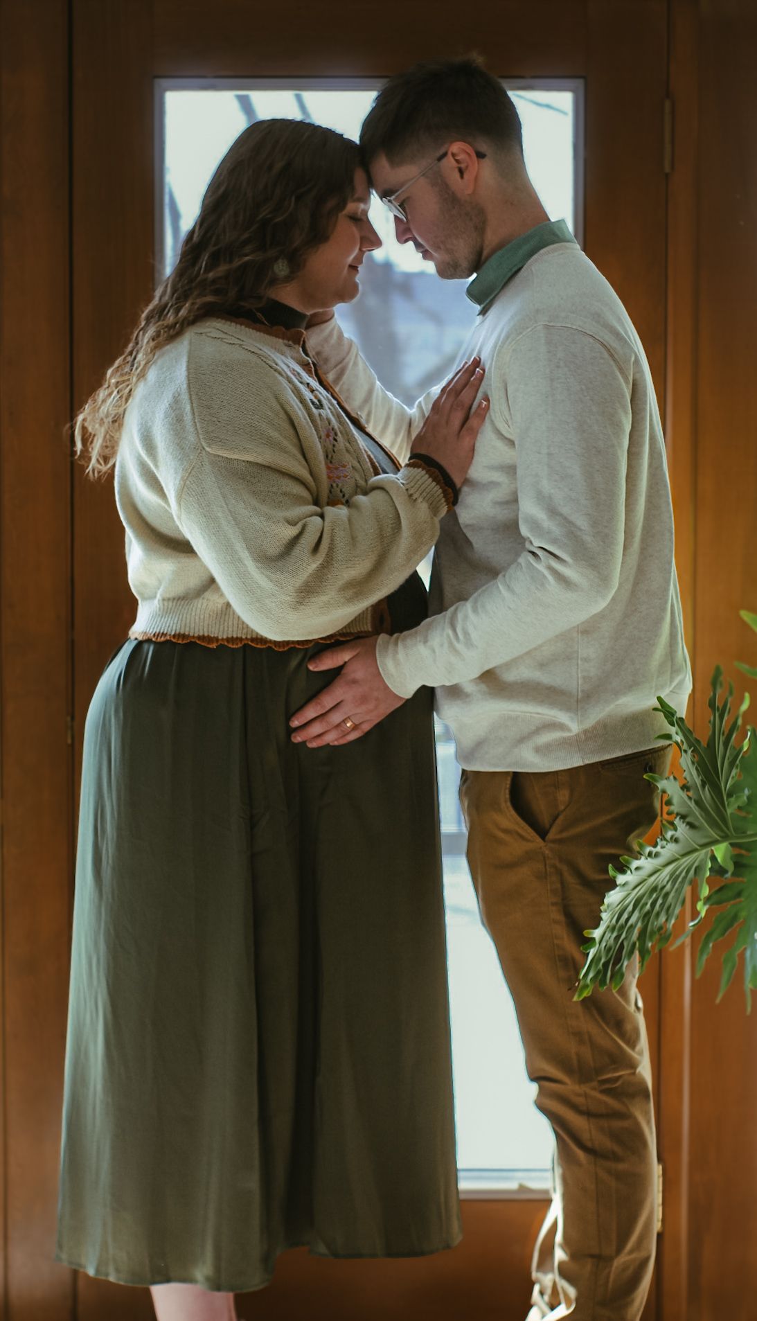 Intimate moment between couple in cream sweaters by window.