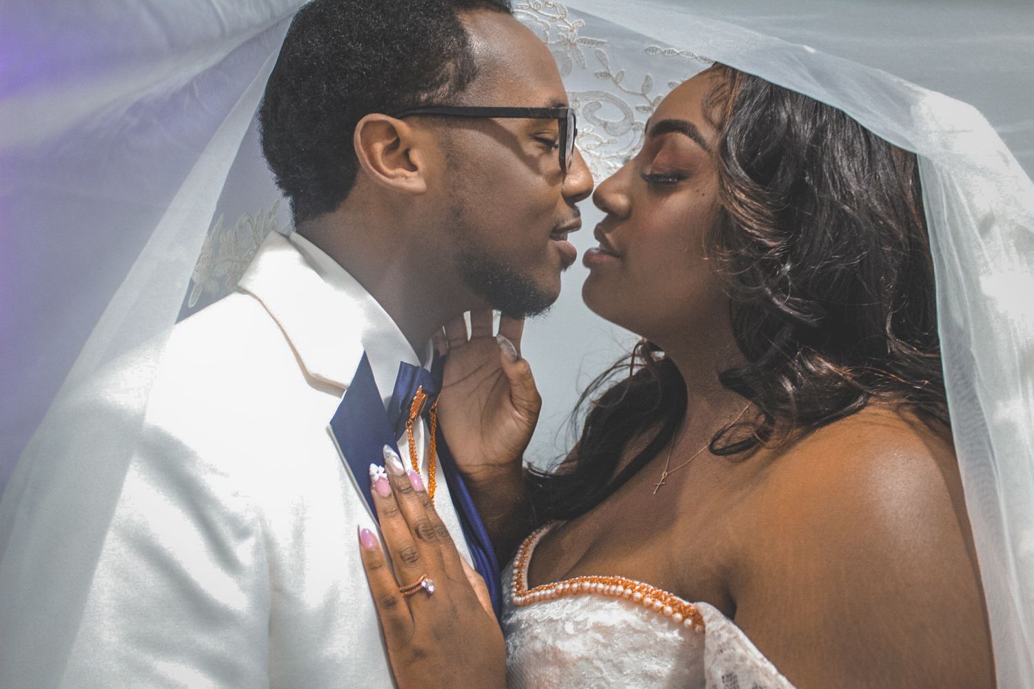 A romantic wedding portrait showing a tender moment between bride and groom beneath a sheer veil.