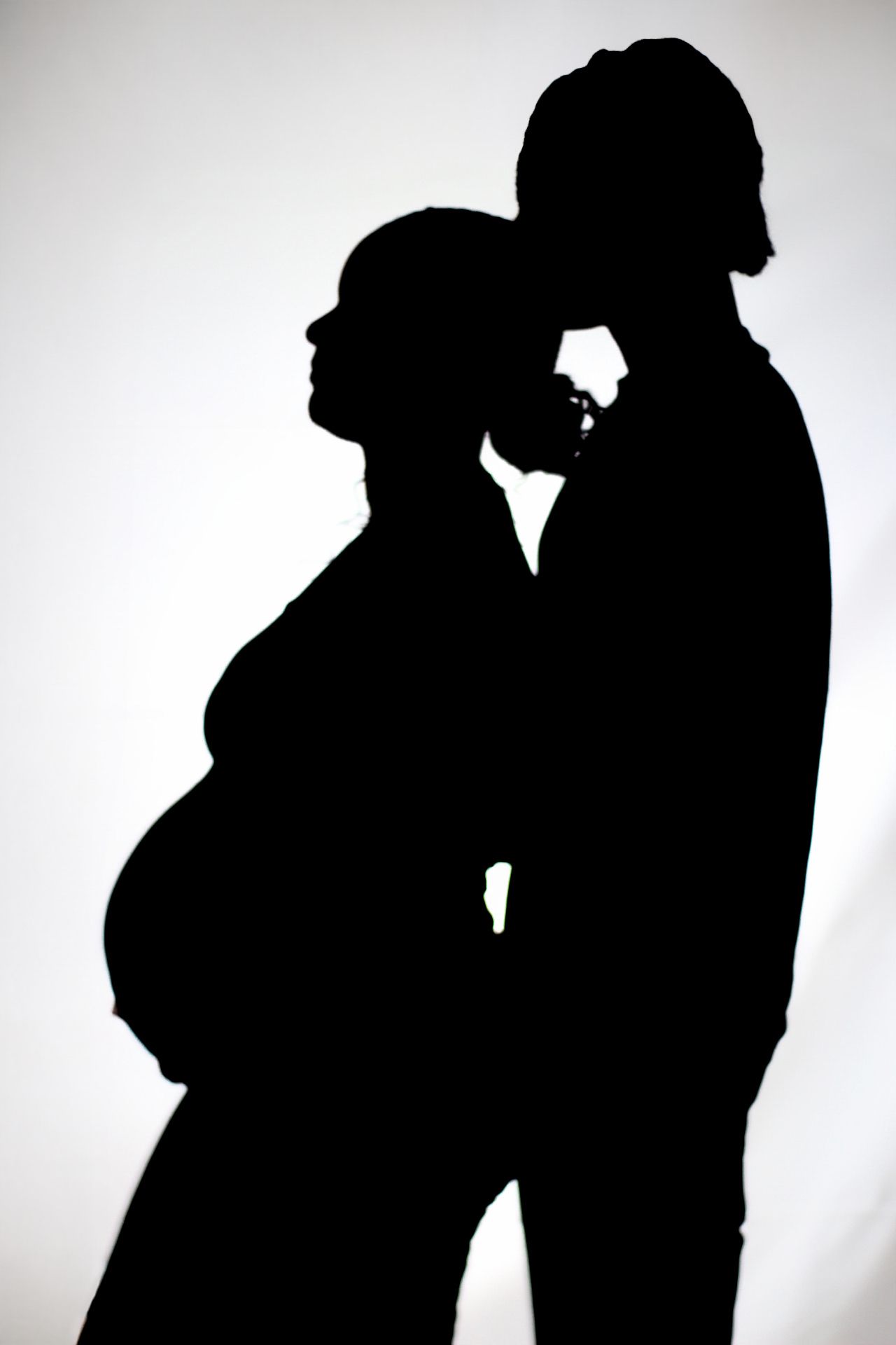 Silhouette of expectant couple embracing against white background.