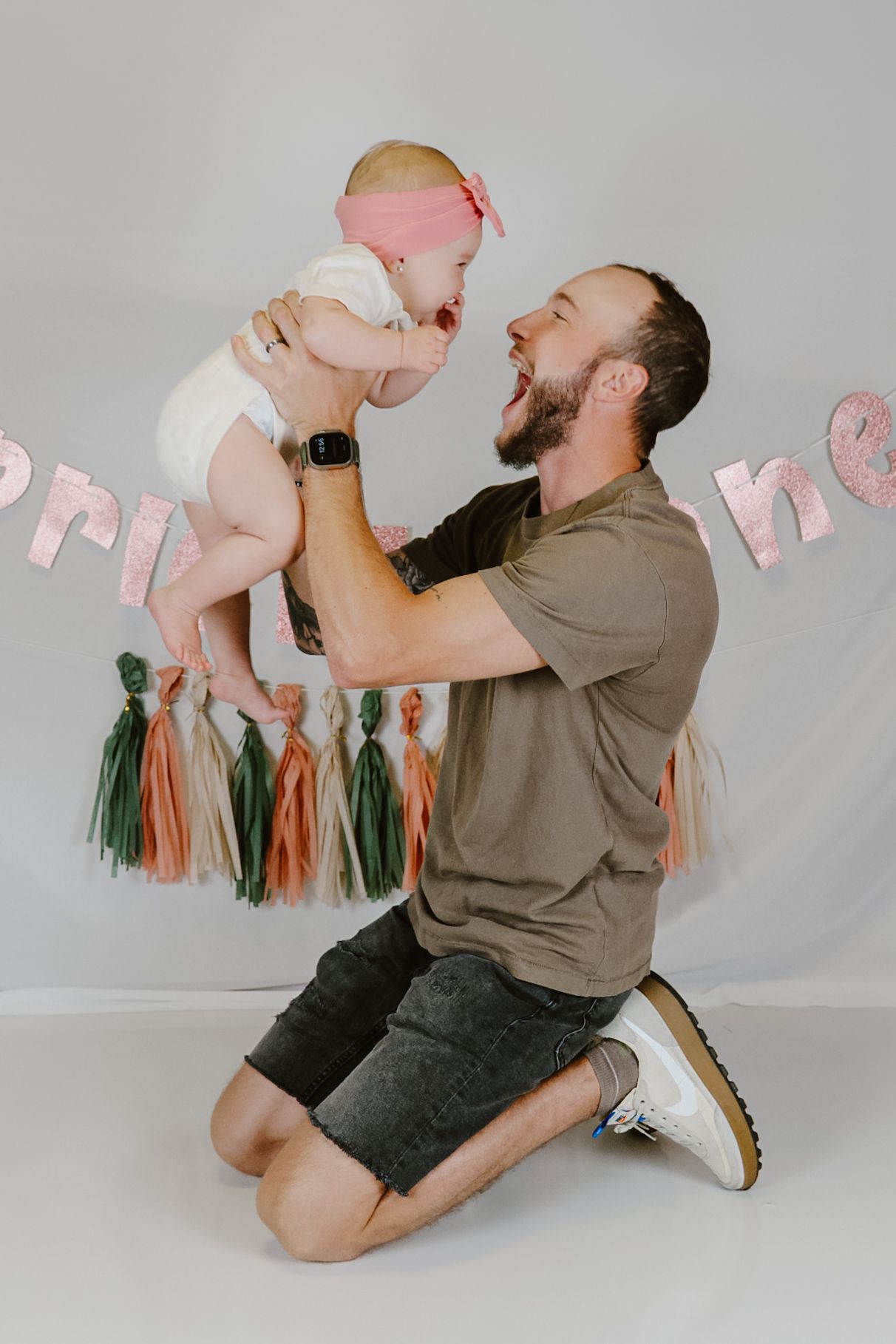 Joyful moment captured against grey backdrop with peach and green tassel garland decorations.