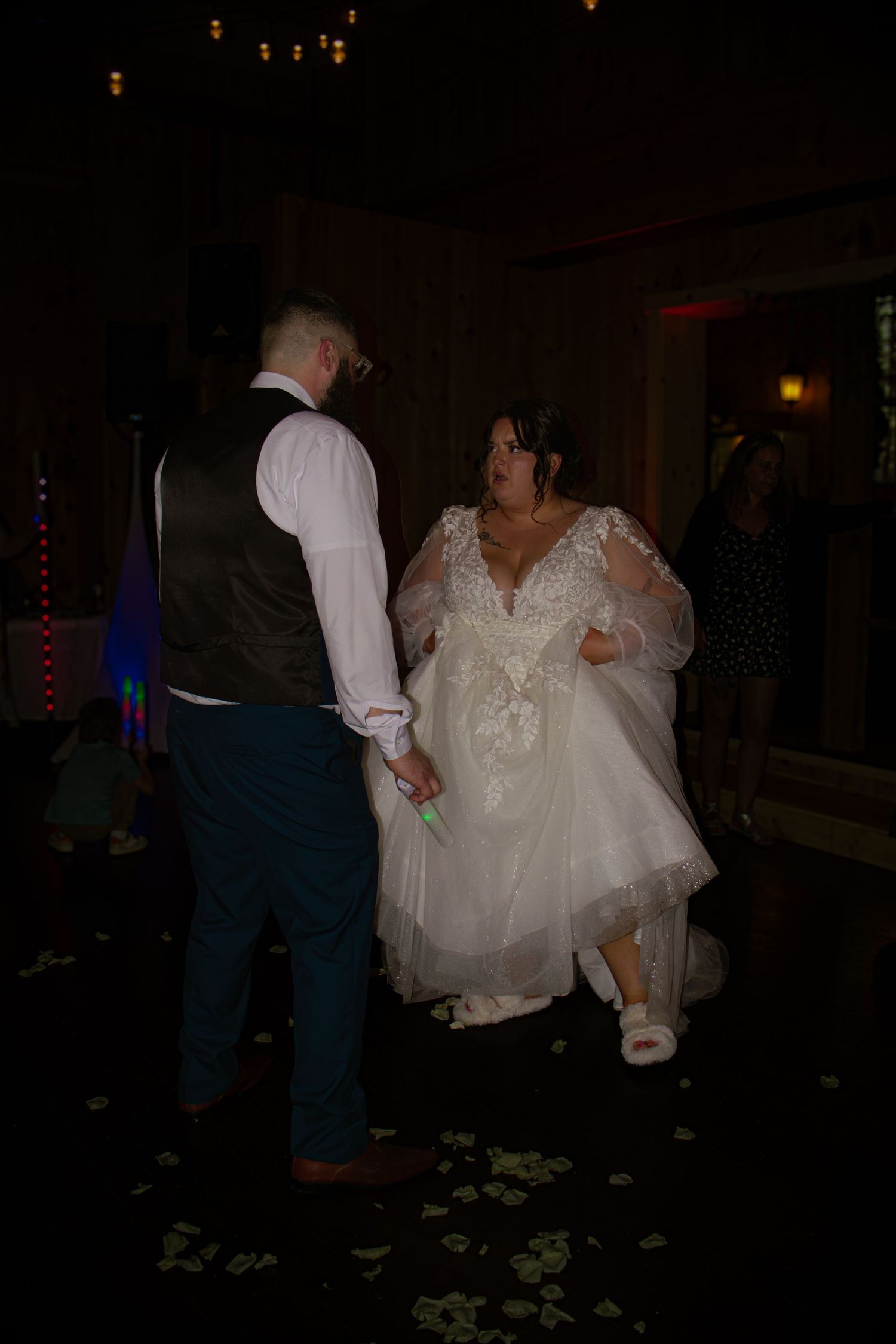 Bride and groom share first dance at wedding reception in dimly lit venue, bride wearing lace gown.