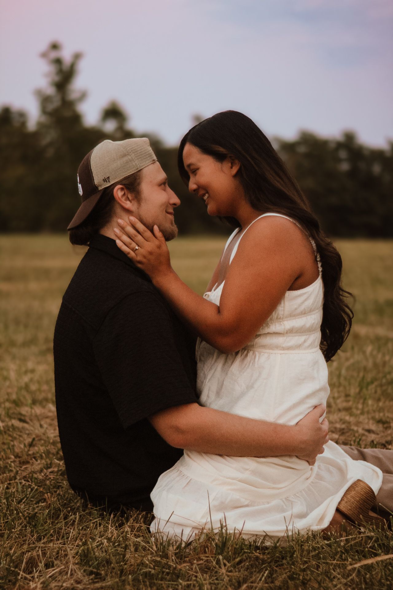 A couple sits together intimately in a grassy field during golden hour, sharing tender moments in a romantic photoshoot.