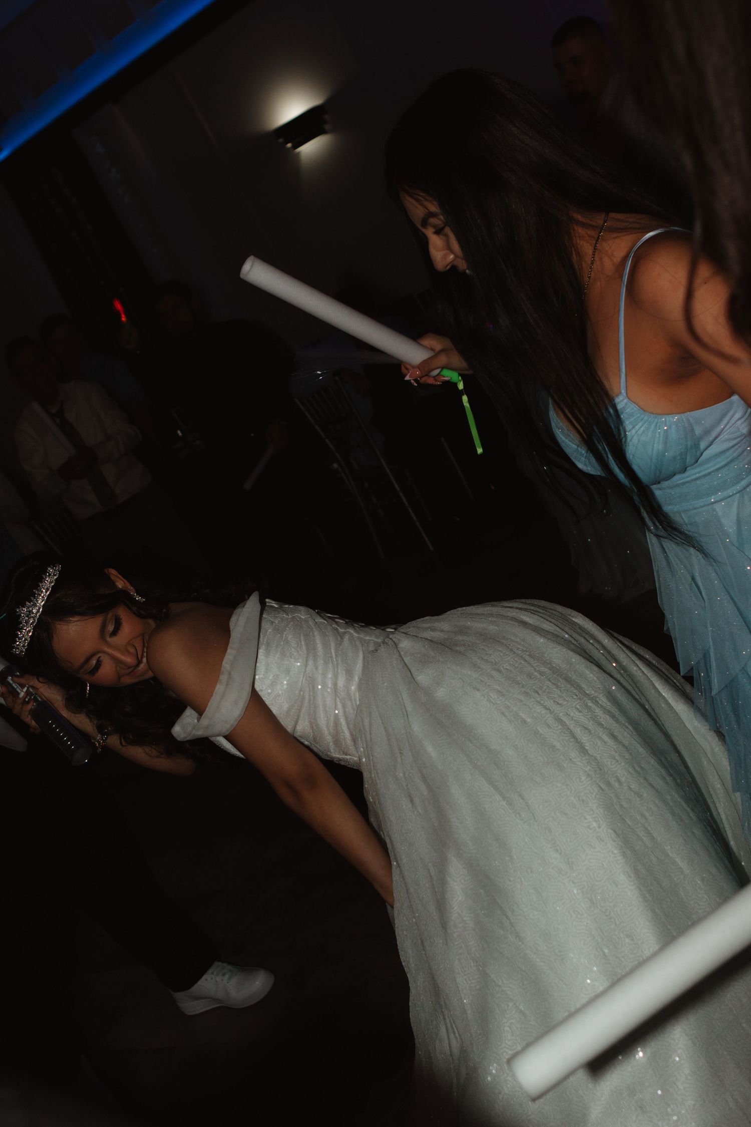 Bride in a white ball gown dances with guests holding glow sticks at a lively wedding reception party.