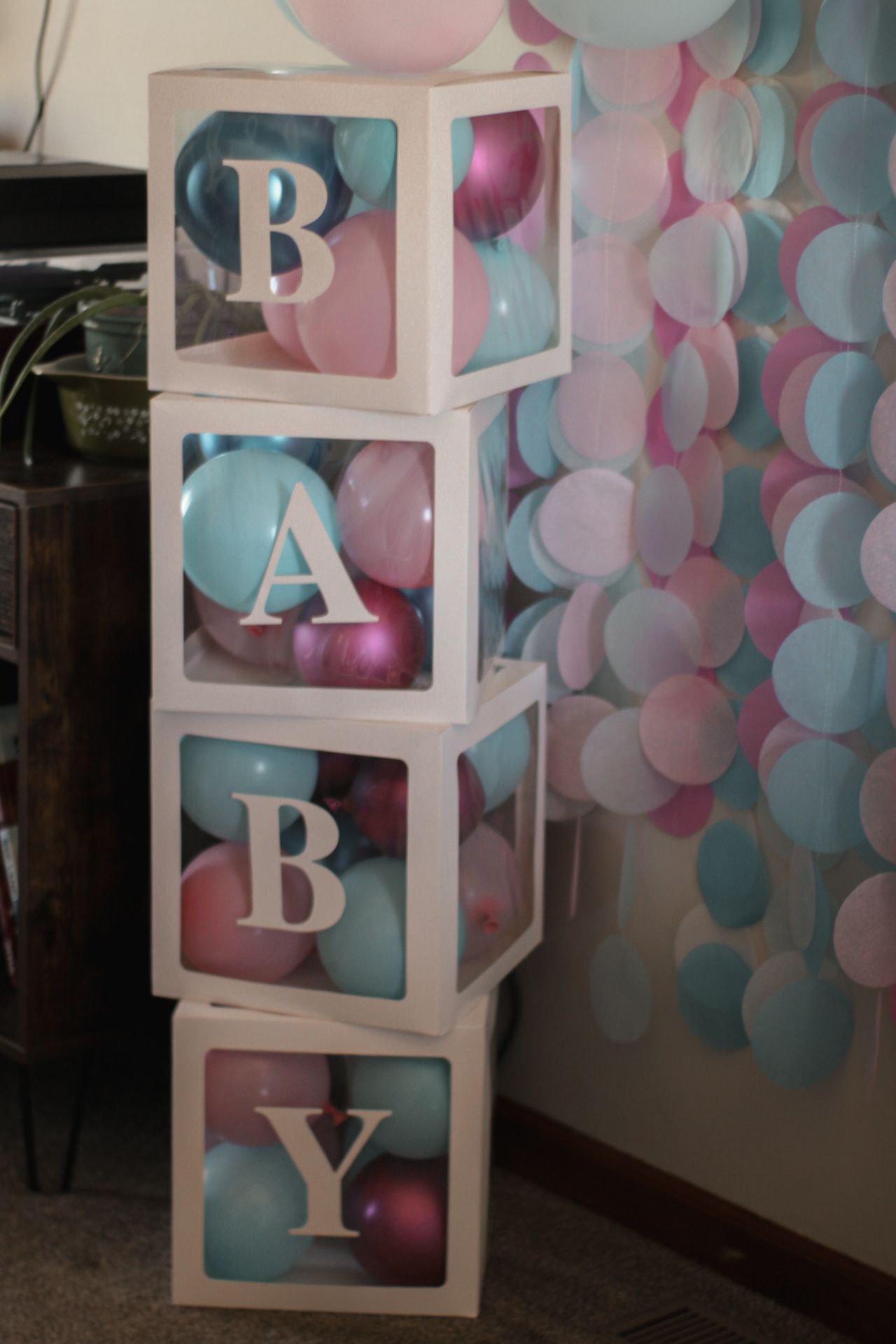 Baby shower decoration featuring white block letters surrounded by pink and blue balloons.