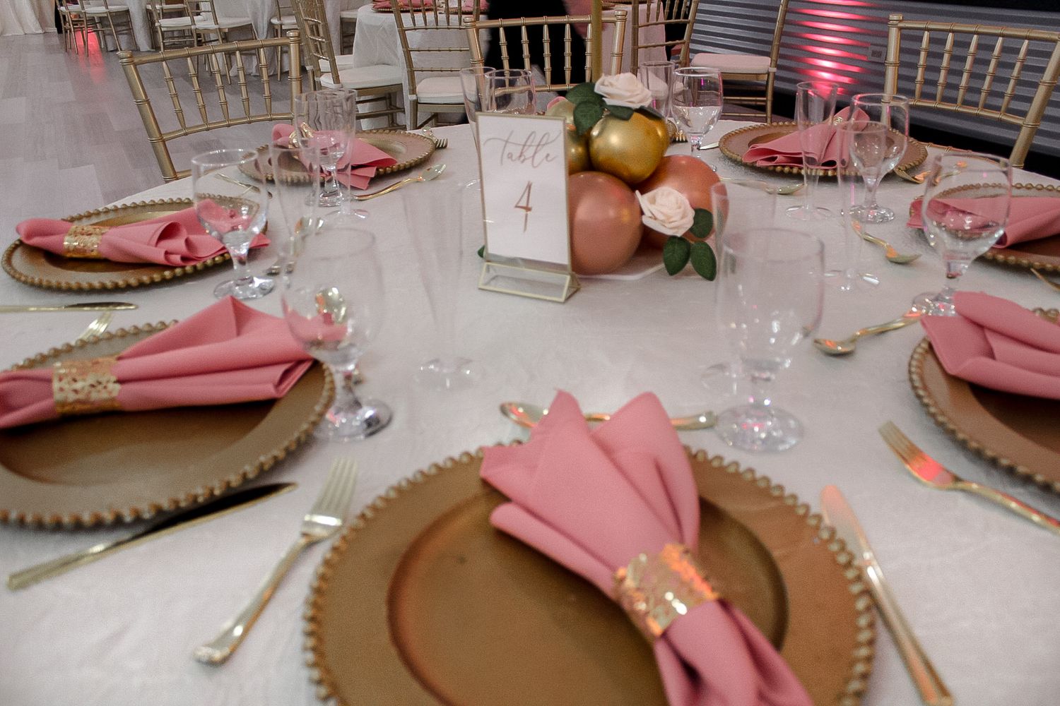 Pink and gold table setting with charger plates, napkins and floral centerpiece.