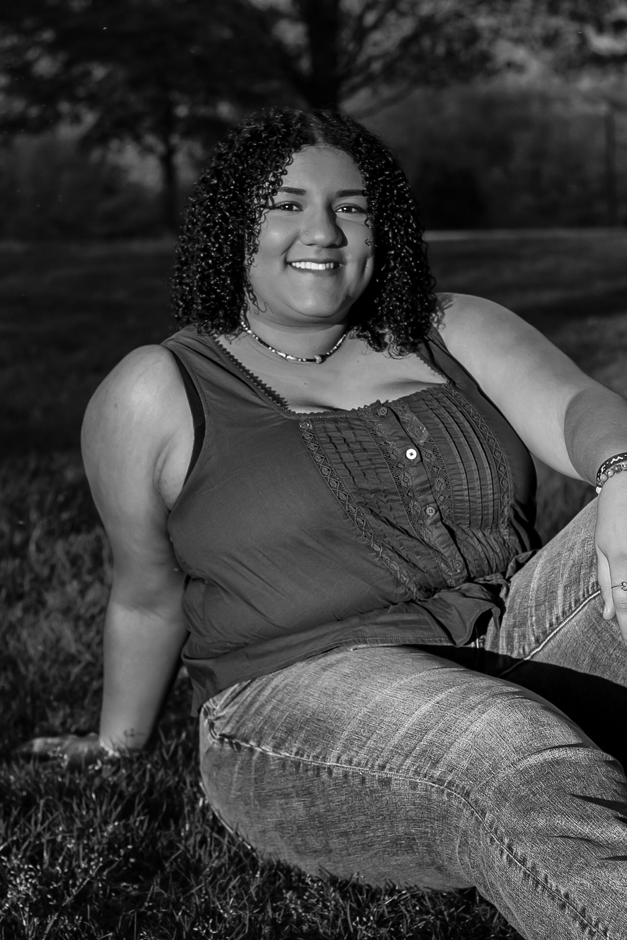 Black and white portrait session of a curly-haired figure laying in grass wearing a dark top.