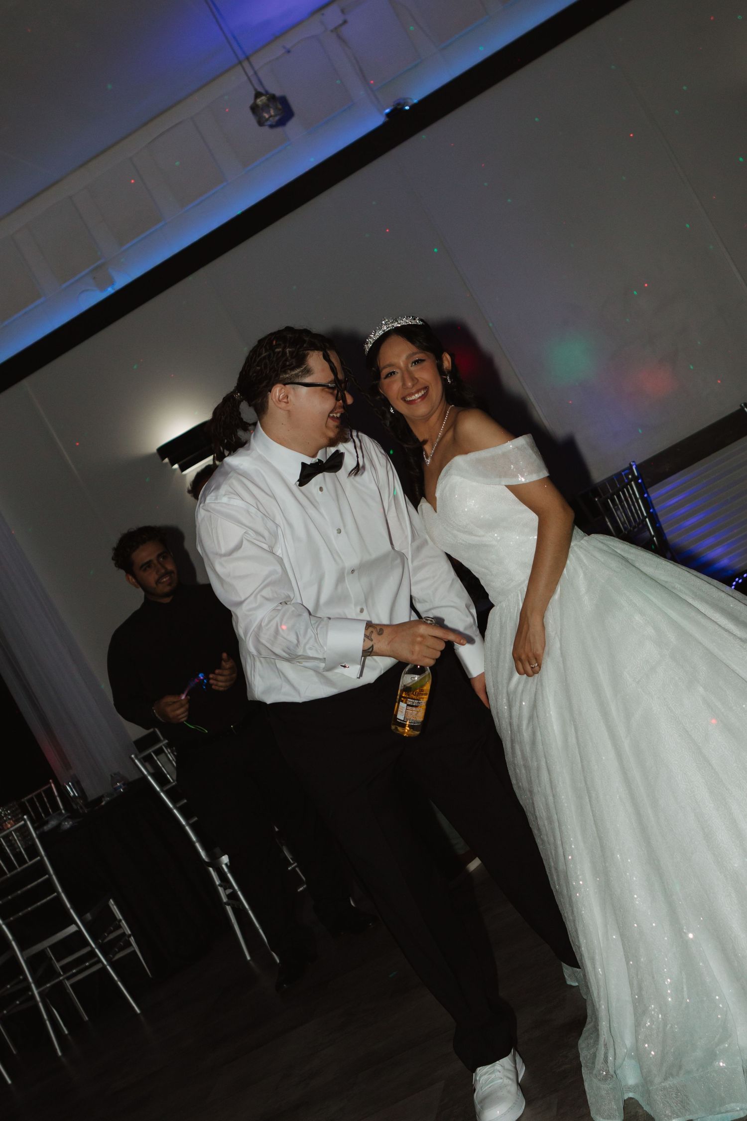 Bride in white gown and groom in white tuxedo dancing joyfully at their wedding reception.