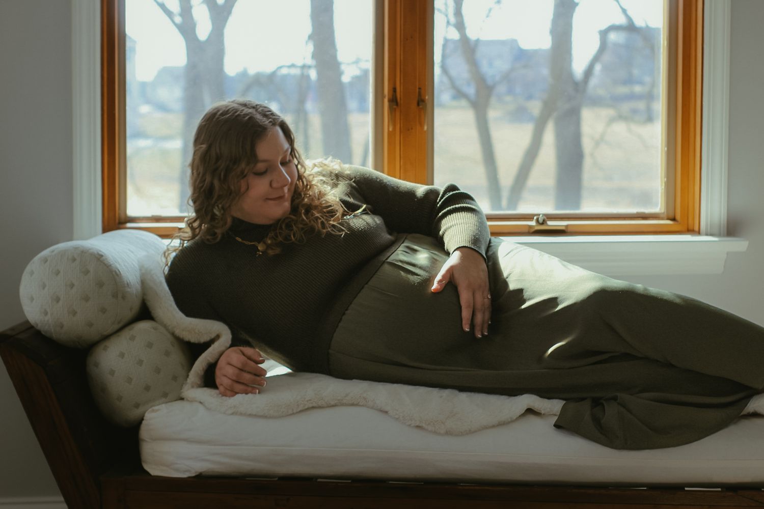 Person relaxing on a couch by a window in casual winter attire.