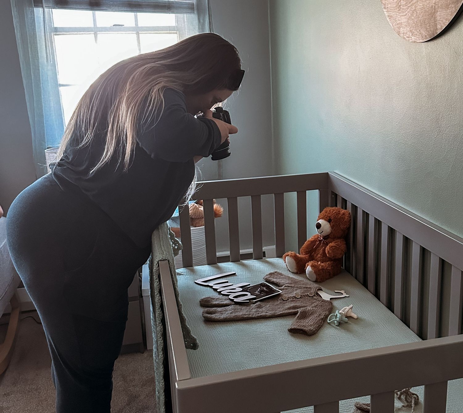 Silhouette of person taking photos over a baby crib with teddy bear.