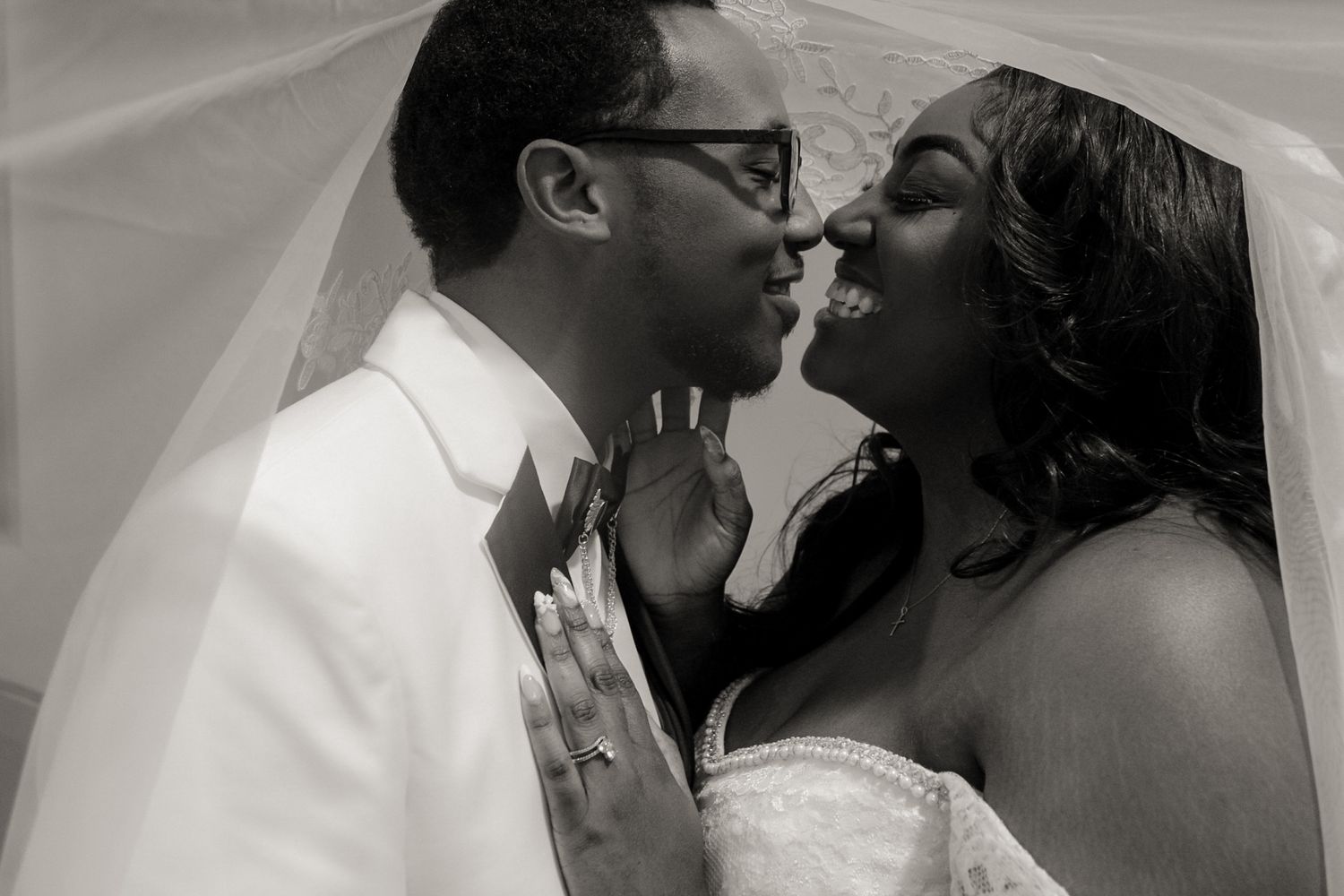 An intimate black and white photo of newlyweds sharing a romantic moment under the bride's veil.