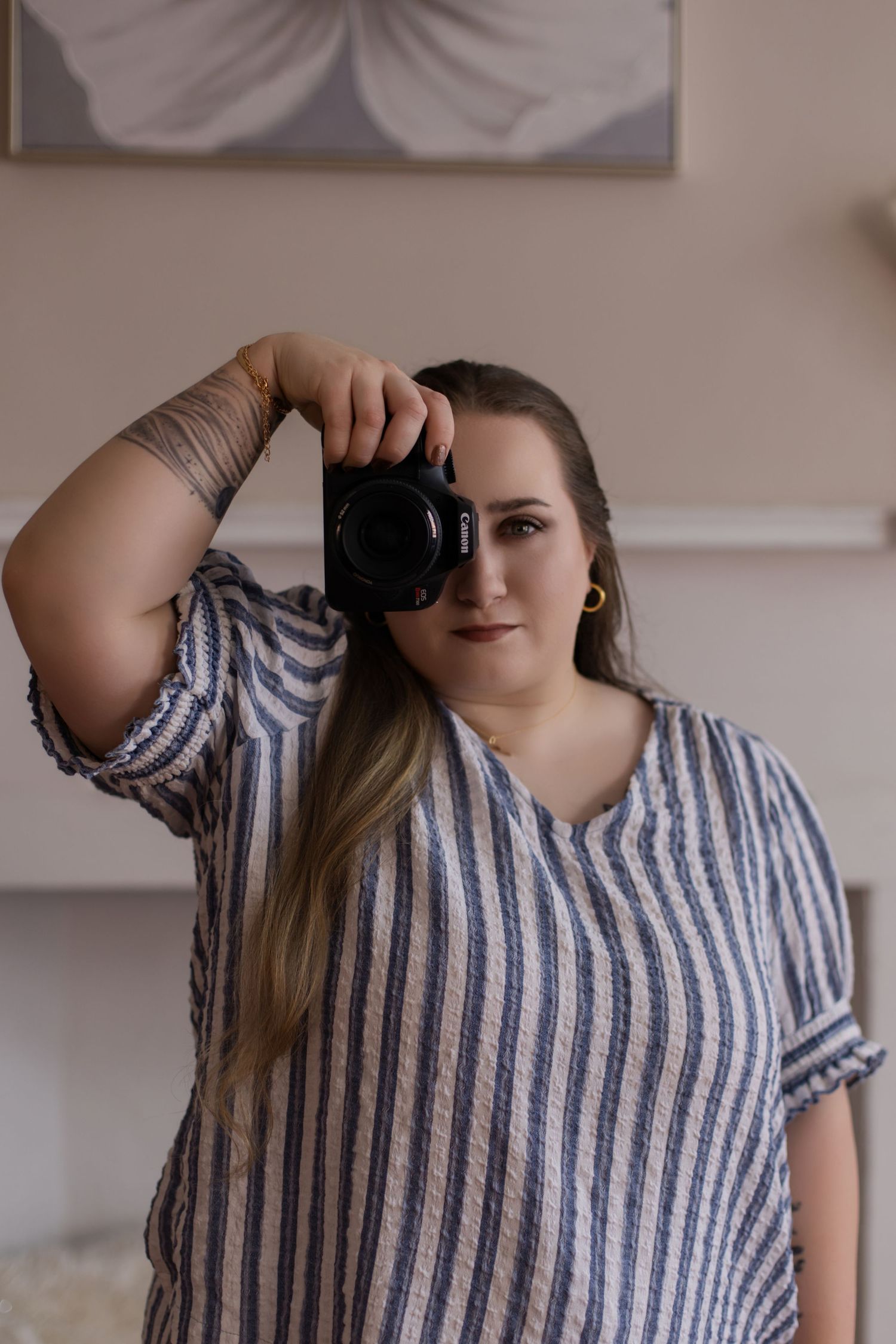Creative self-portrait of photographer holding camera in striped outfit against neutral backdrop.