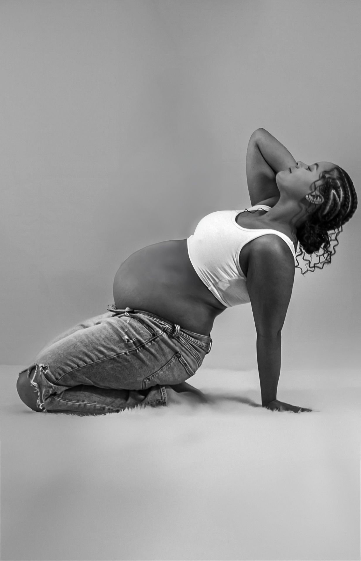 Black and white portrait of pregnant person in casual attire doing yoga pose on floor.
