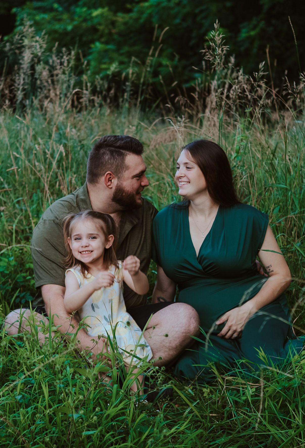 A joyful family moment captured in tall grass during an outdoor maternity photo session.