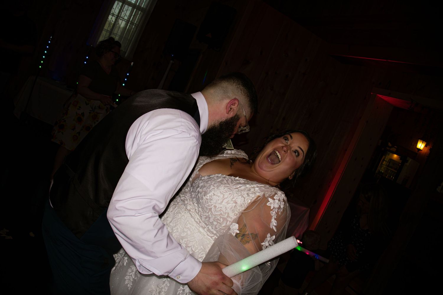 Bride and groom share a romantic dance at their wedding reception, with colorful lights in the background.