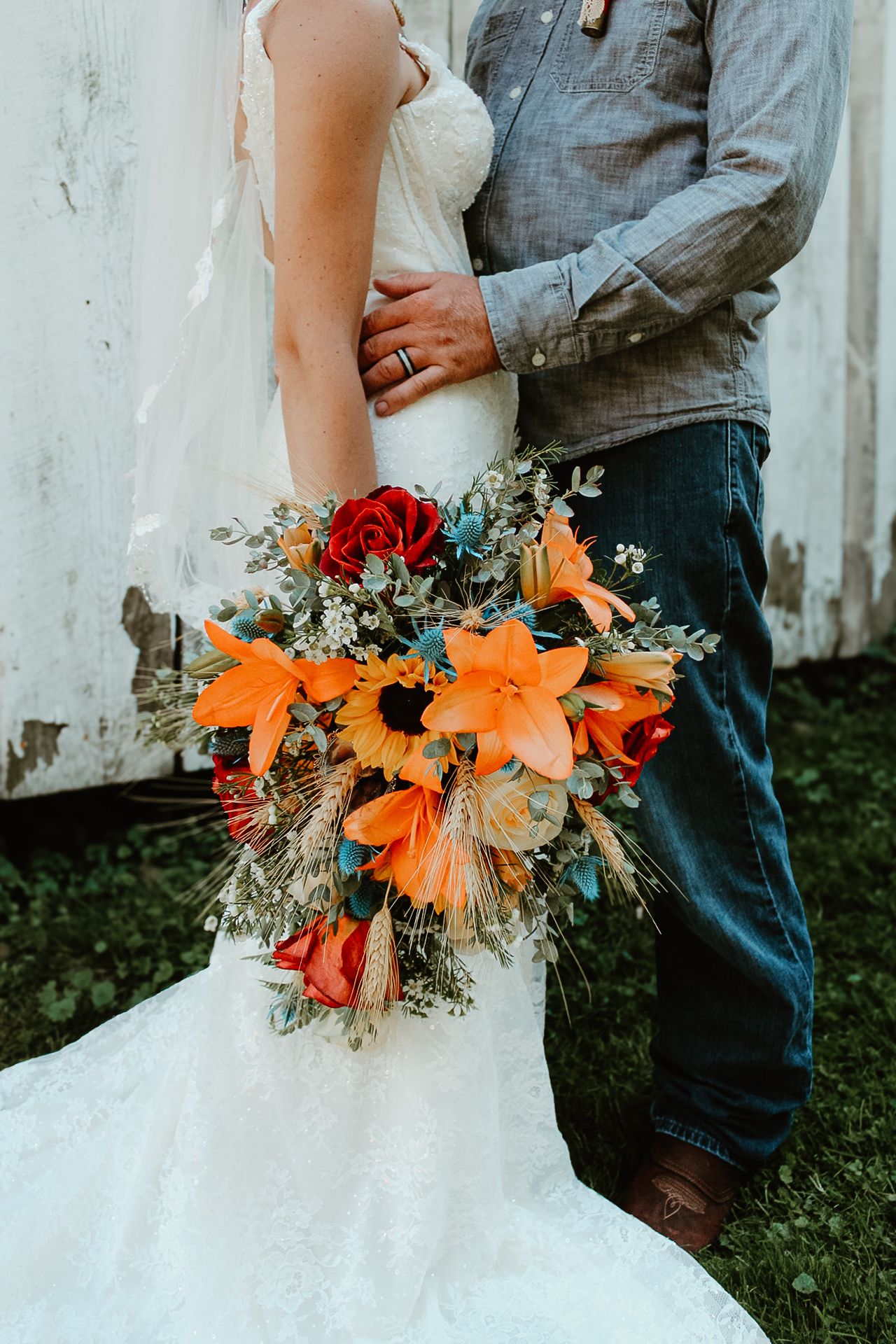 A bridal bouquet with vibrant orange lilies, red roses and white flowers against a white wedding dress.