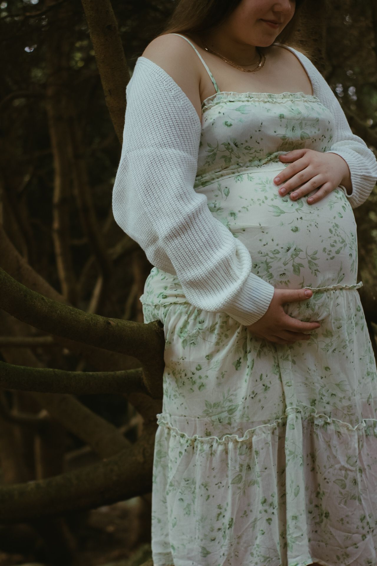 Side view of a pregnant belly in a flowing floral dress with white knit sweater.