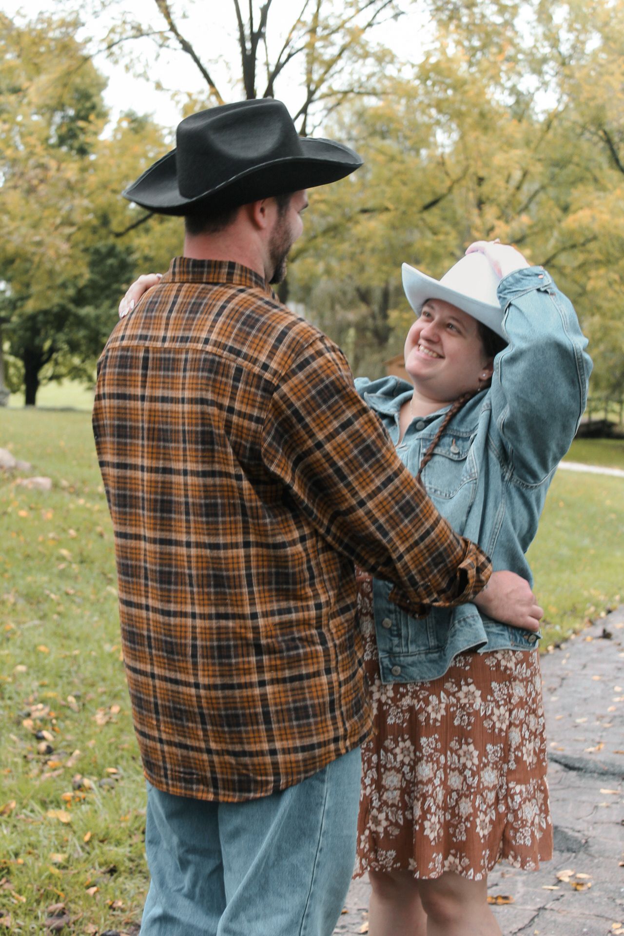 Playful couple in western hats sharing tender moment on autumn path.