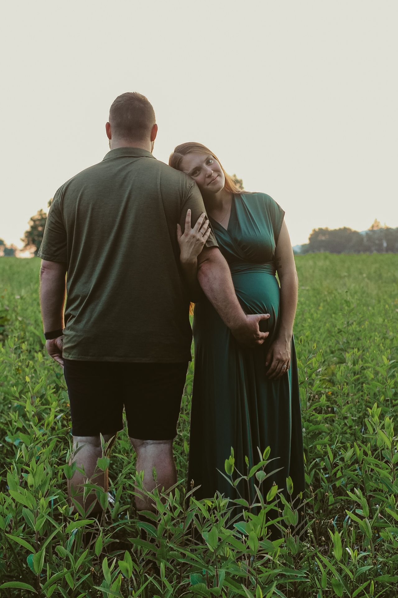 Intimate moment shared between a couple sitting in a lush green field at sunset.