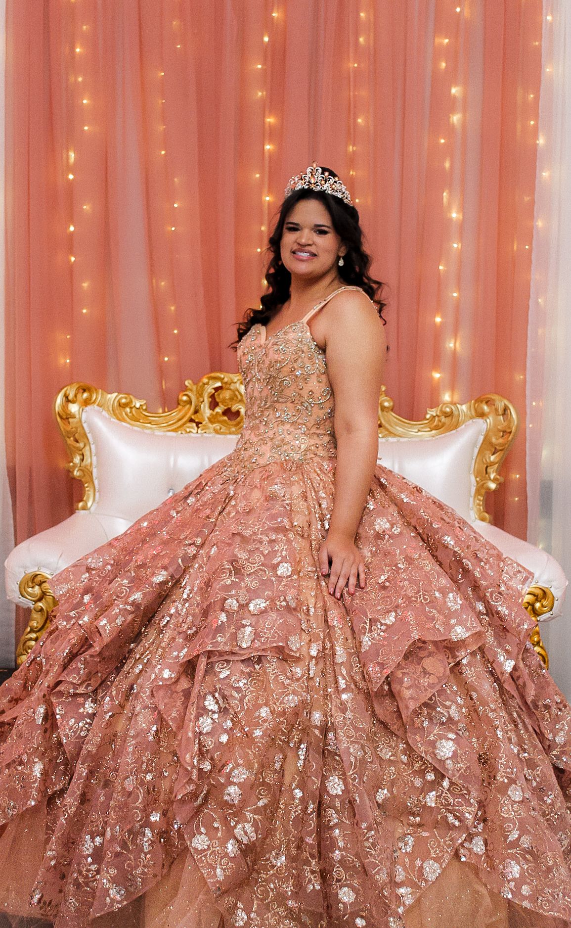 Full-length portrait showcases detailed rose gold ballgown with floral appliques against pink backdrop.