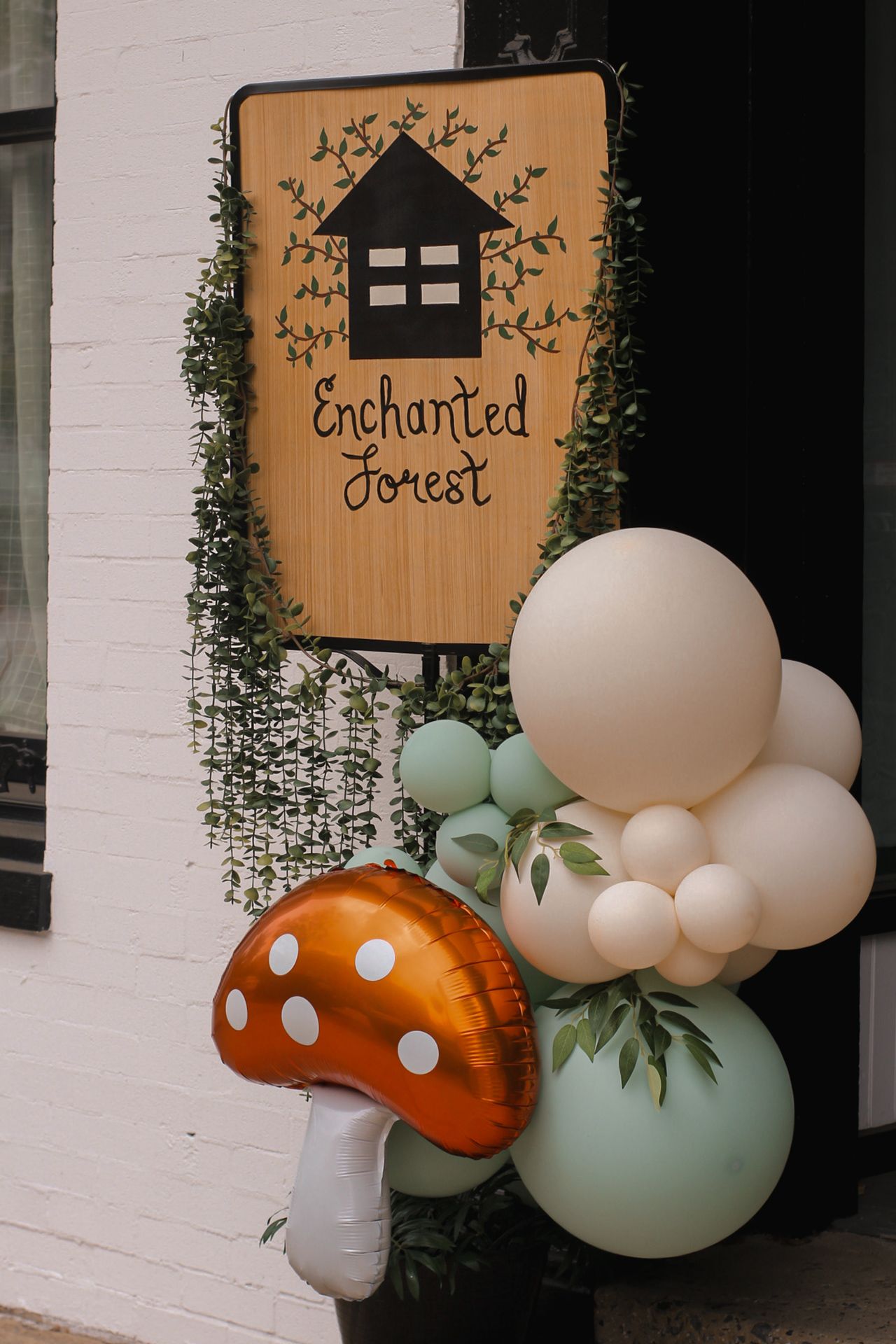 Enchanted forest themed party decoration with mushroom balloons and greenery.