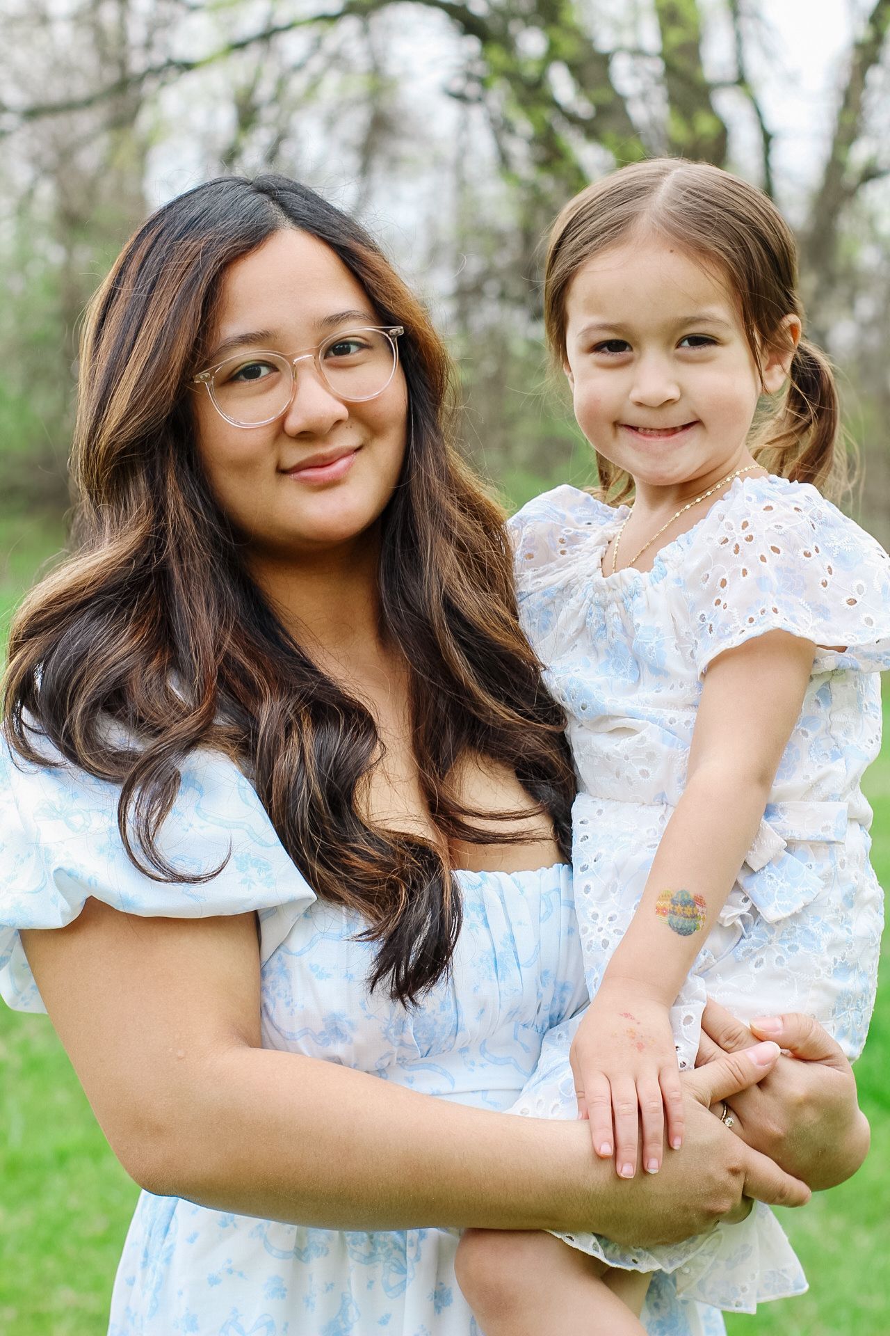 Mother and daughter wearing matching white lace sundresses pose together outdoors in springtime.