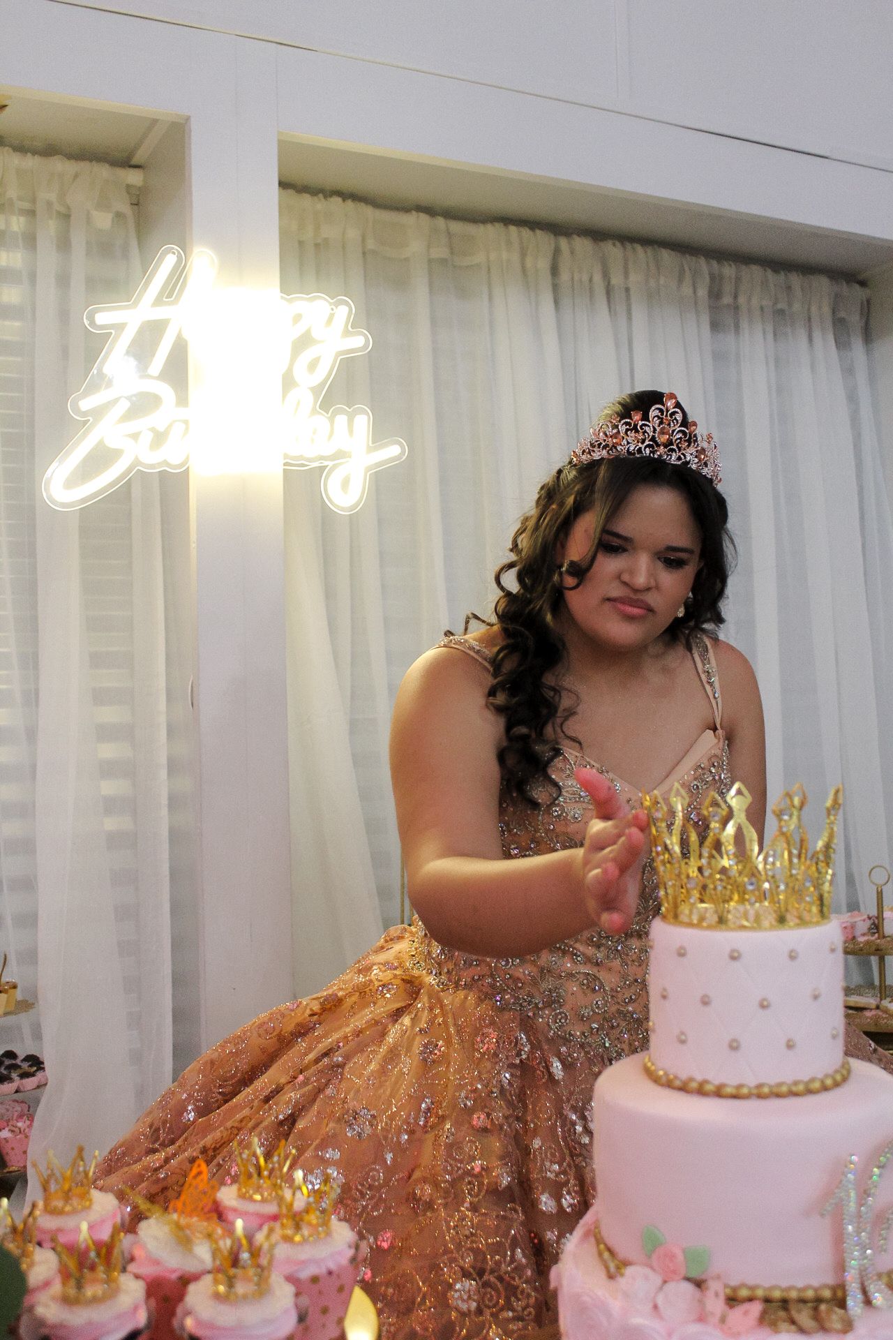 Celebration features tiered pink and gold crown cake with guest in sparkling formal attire.