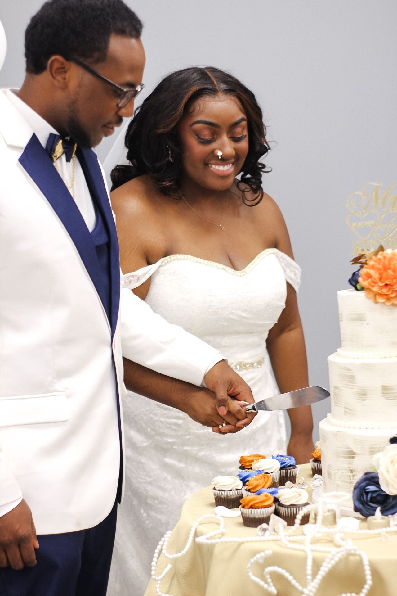 Newlyweds cutting their wedding cake decorated with orange and navy accents.