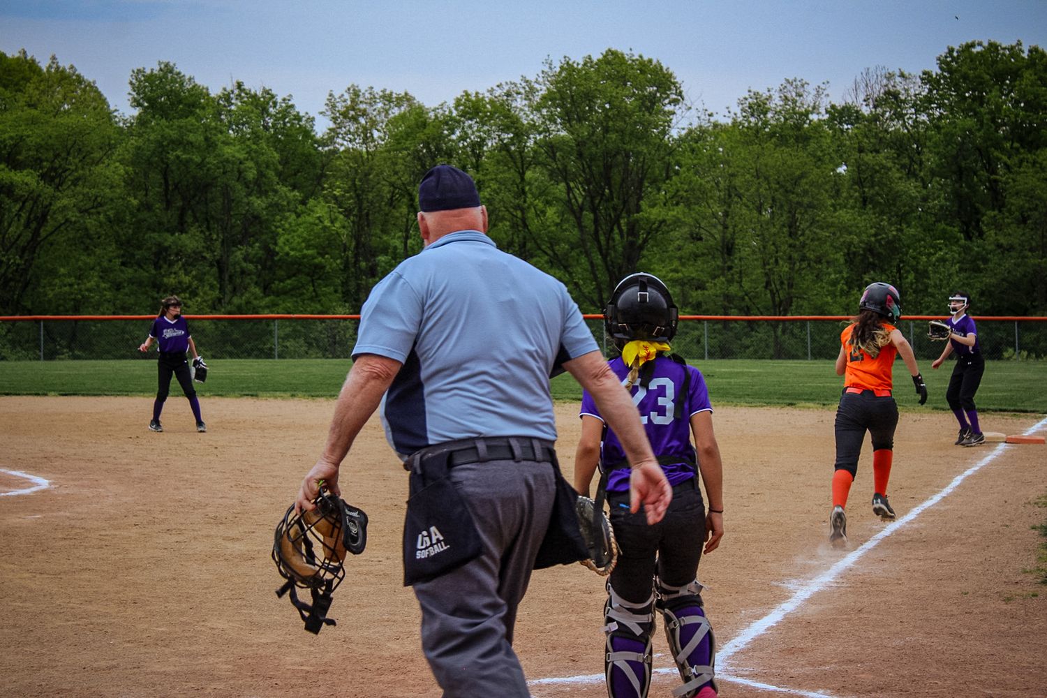 Umpire observes softball game action at home plate during active play.