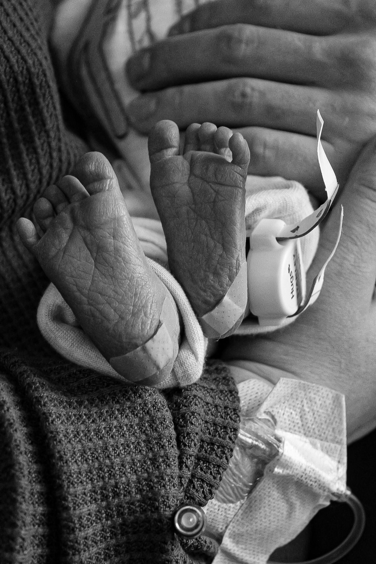 Black and white close-up of tiny newborn baby feet against a knit blanket.