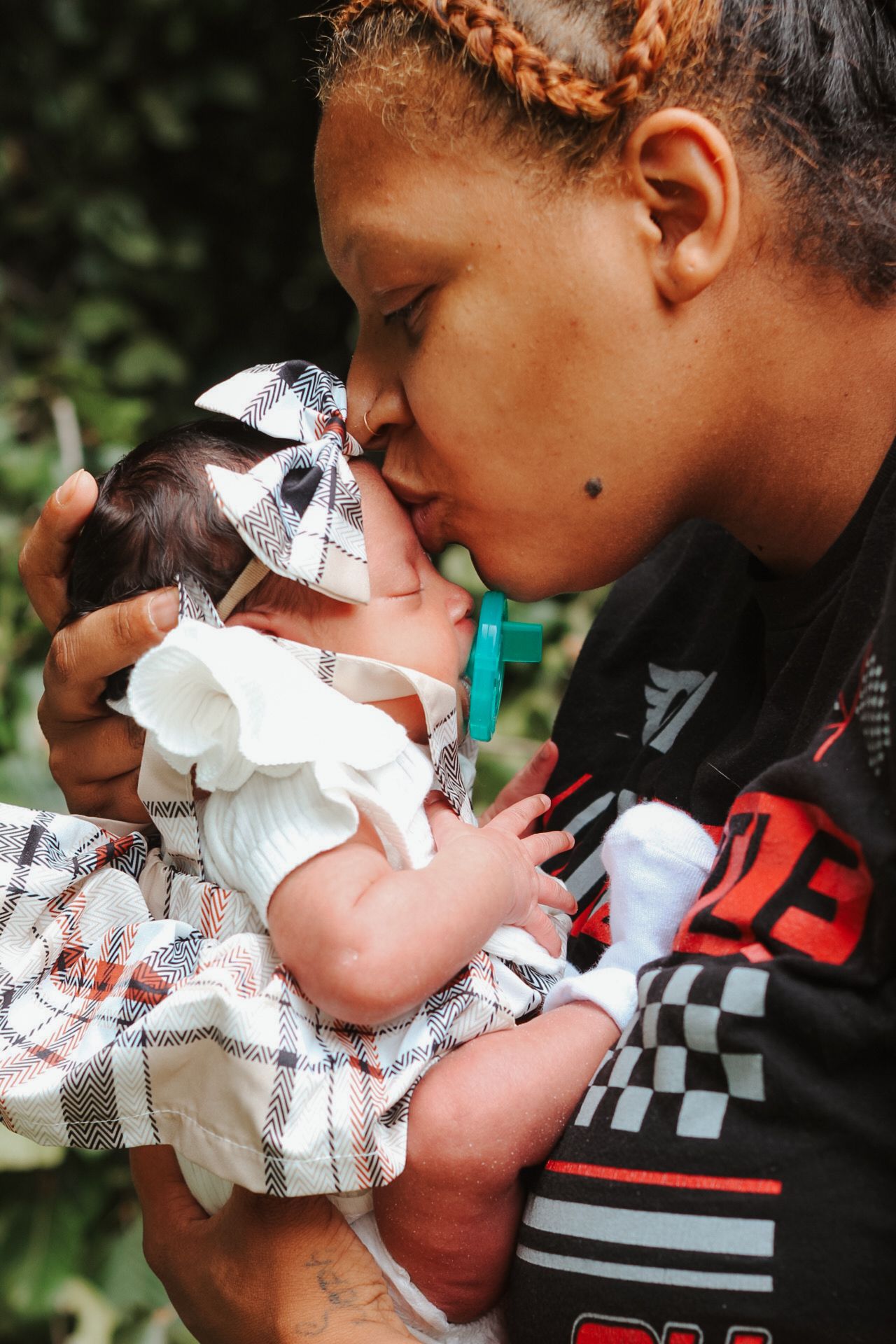 A tender moment shared between parent and newborn baby wearing a plaid outfit and bow headband.